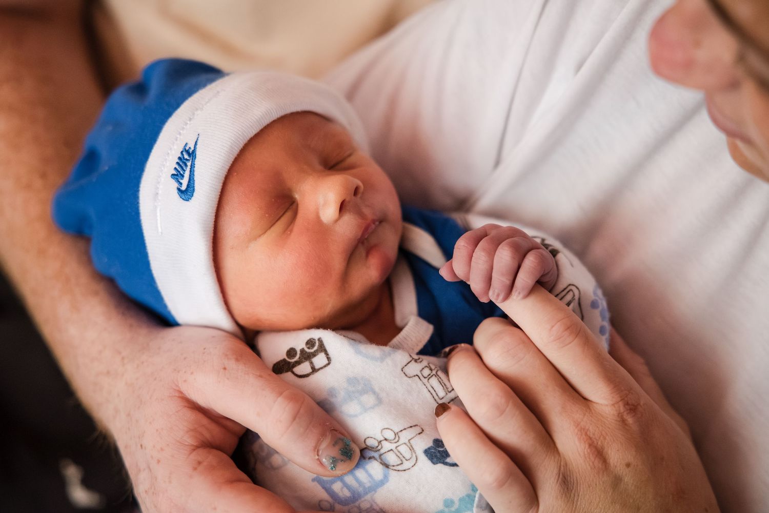 Newborn baby sleeping peacefully in a Nike hat, cradled in loving arms.