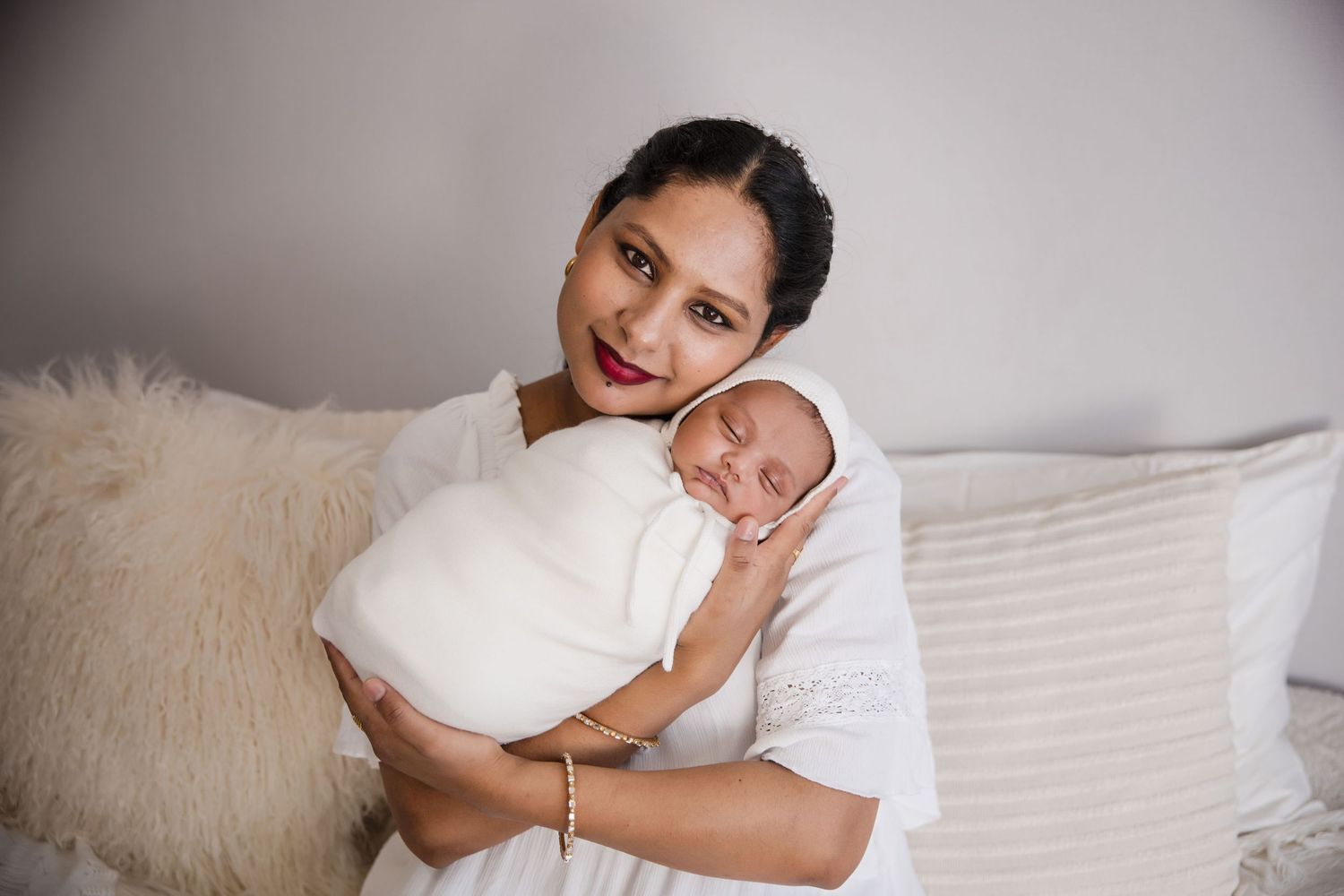 A tender moment as a baby swaddled in white rests against soft pillows.