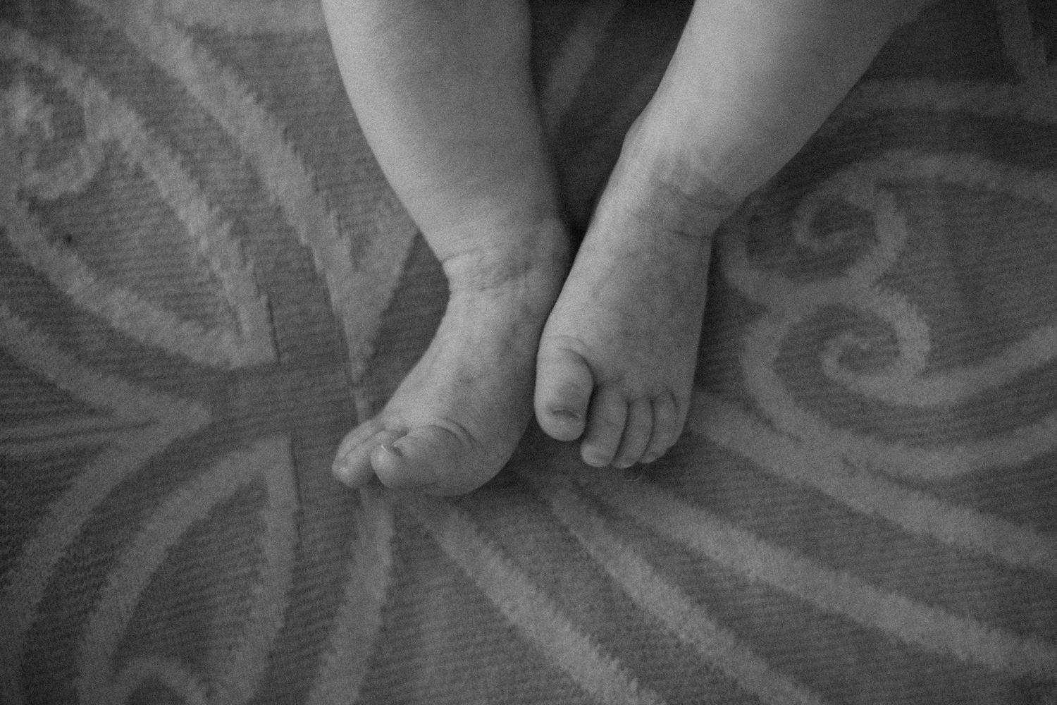 Close-up black and white photo of tiny newborn baby feet resting on a patterned blanket.