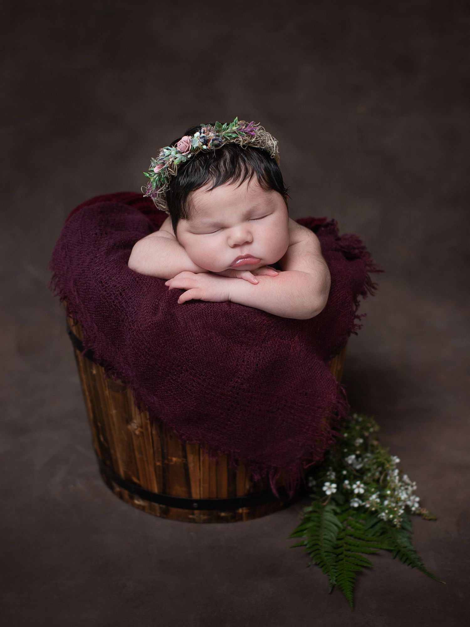 Sleeping newborn with floral crown posed in rustic wooden barrel with burgundy fabric. Cambridge Waikato NZ Photographer