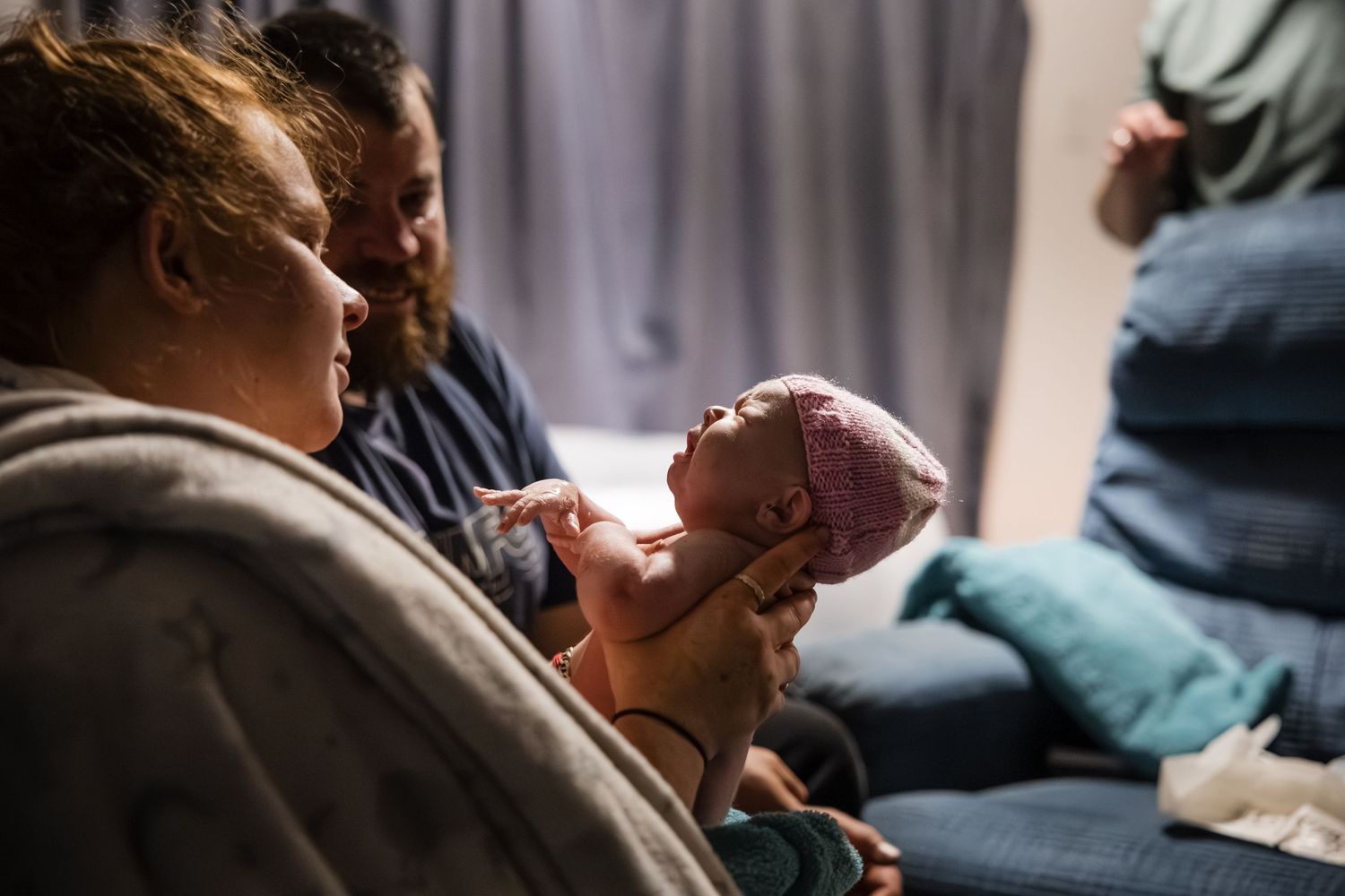 A newborn baby yawns while being cradled in a caregiver's arms during a tender moment at home.