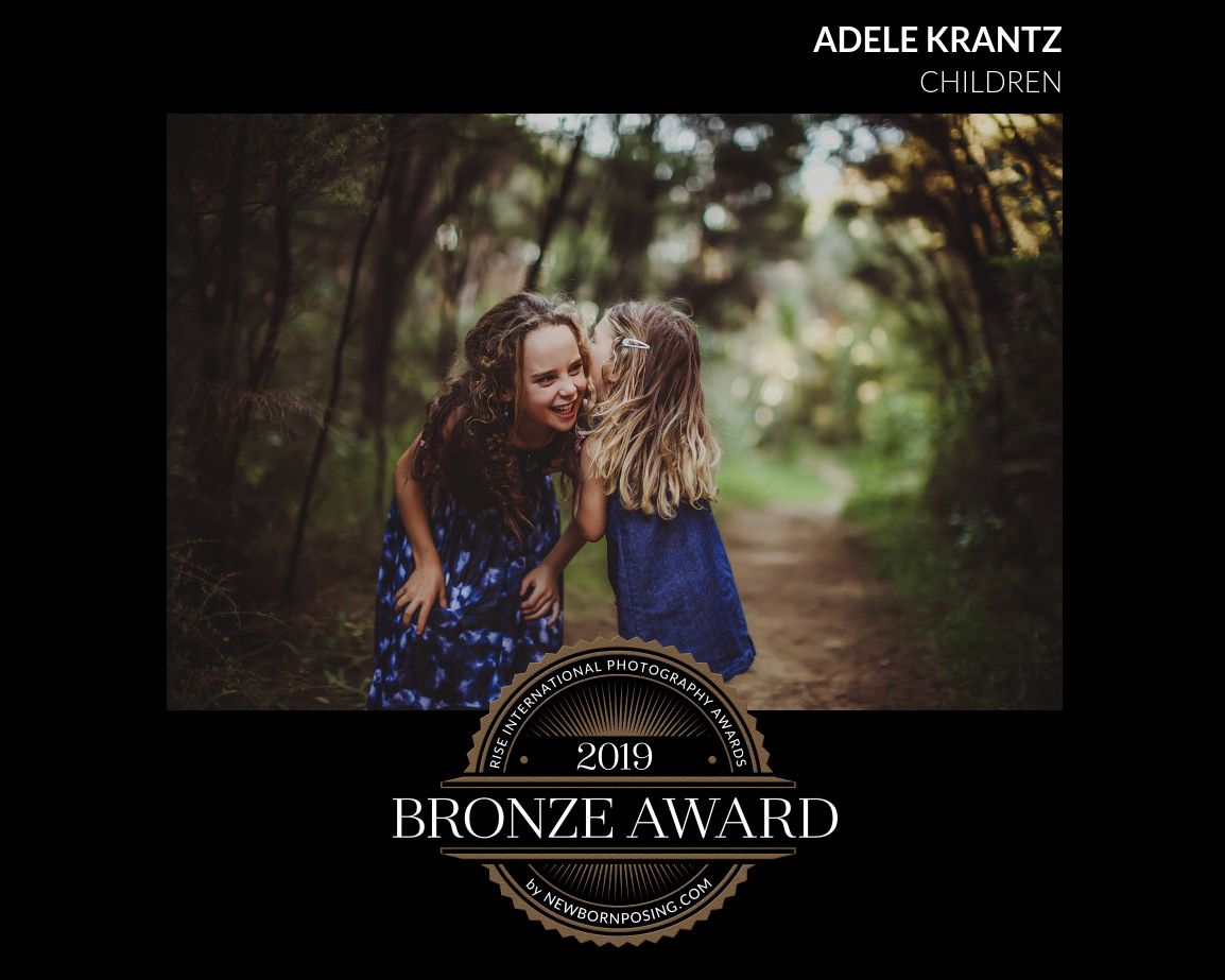 A 2018 bronze award winning portrait photograph shows a warm moment between two people on a wooded path.