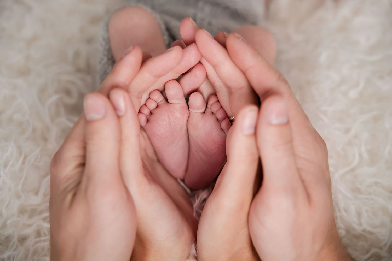 Gentle hands cradle a sleeping newborn baby wrapped in soft white blankets.