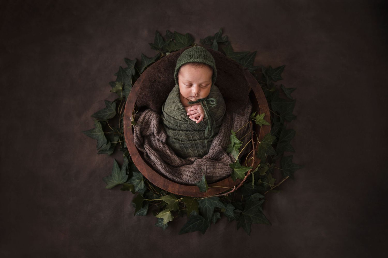 A collection of newborn photos featuring cozy brown wraps and rustic green foliage accents in warm lighting.