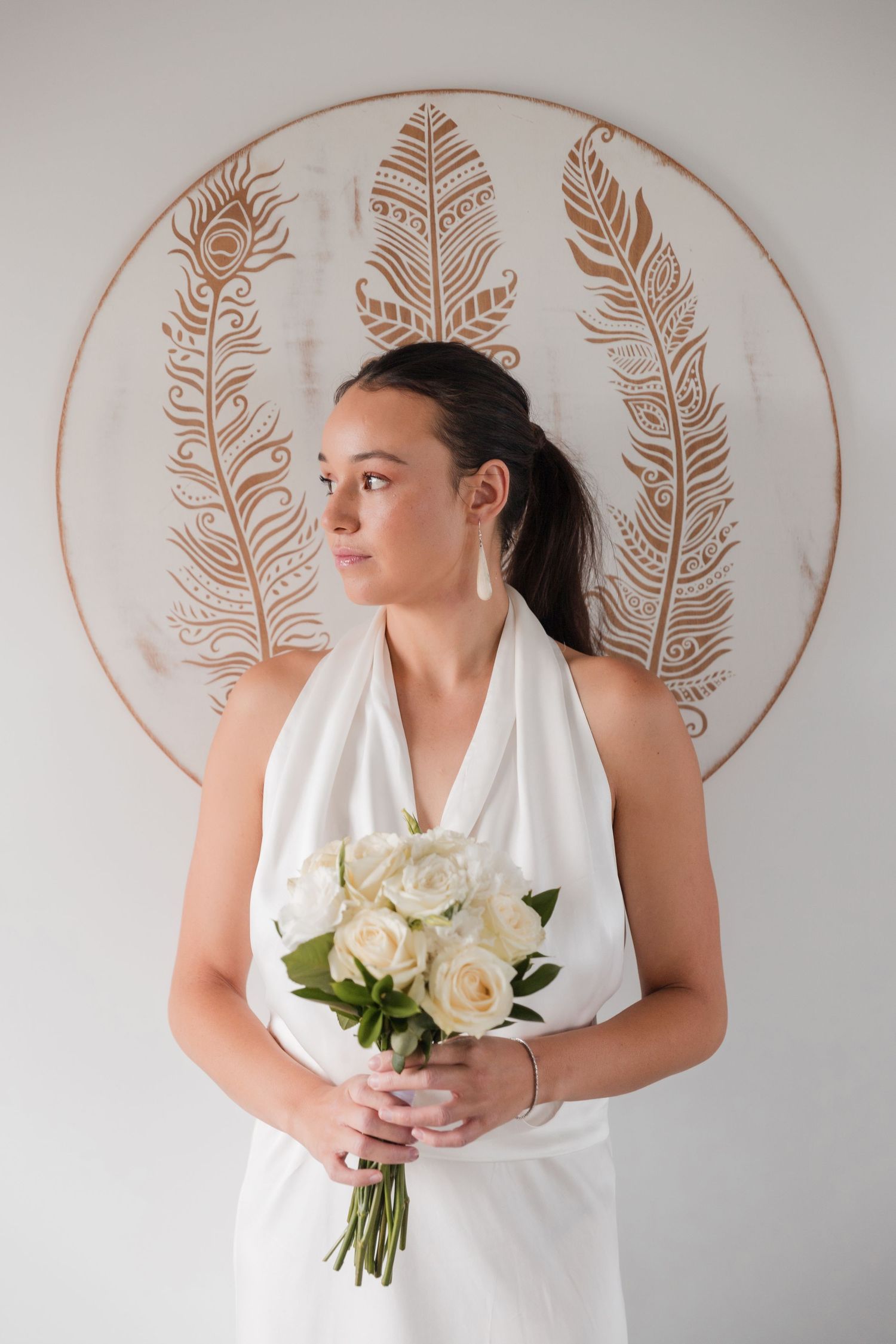 Series of elegant bridal portraits against white wall with copper feather design holding white rose bouquet.