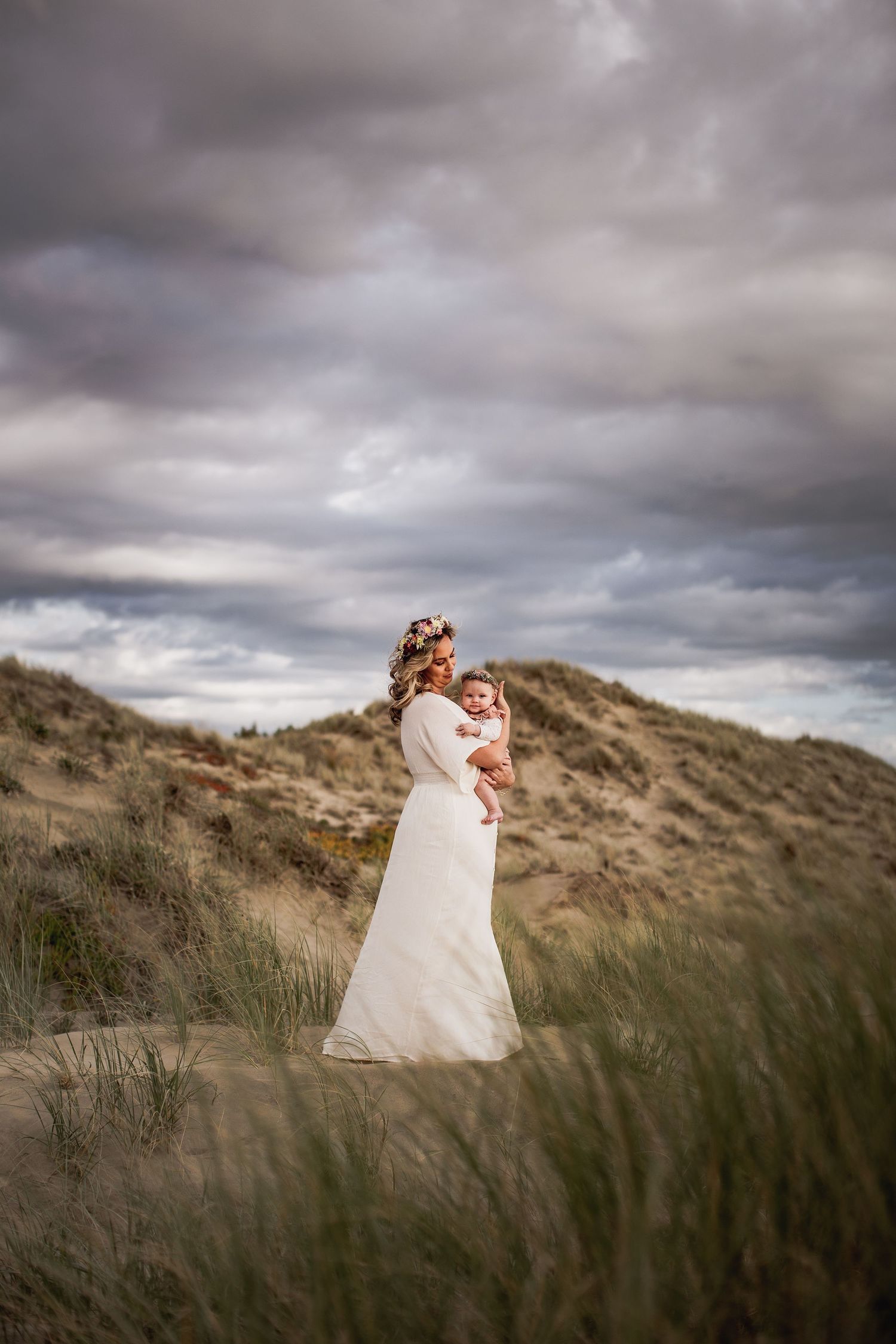 Dramatic coastal portrait of mother and child against stormy sky and sand dunes.