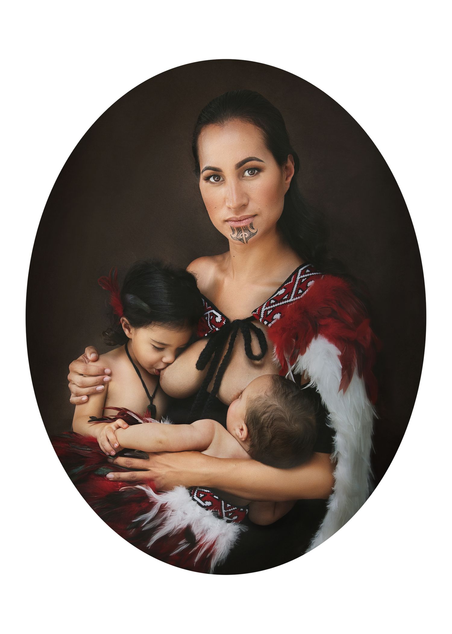 Maori woman with ta moko facial tattoo wearing red feather cloak, breastfeeding infant while holding young child.