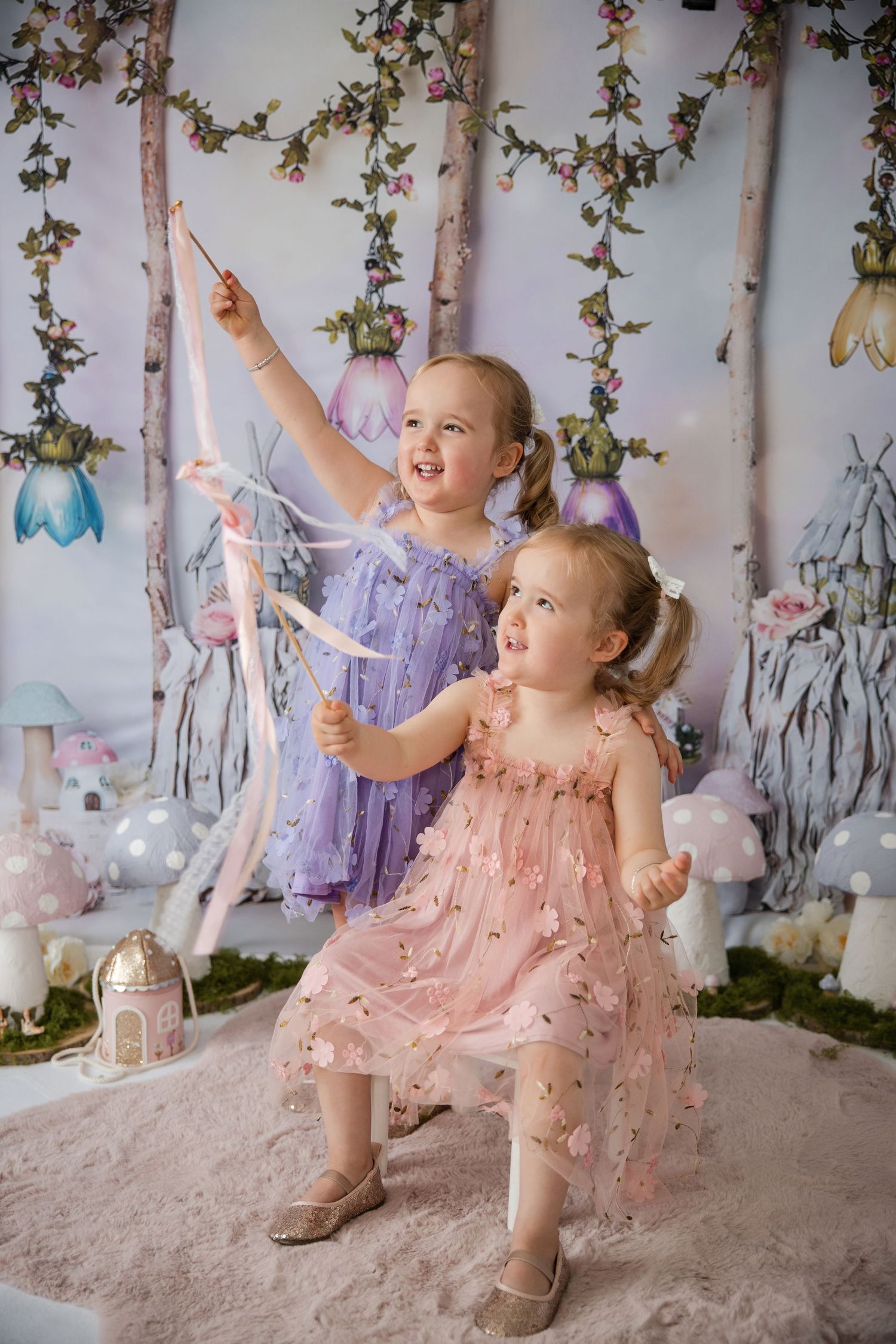 Two little girls in purple and pink tulle dresses play with ribbons in a magical fairy tale themed photo setting.