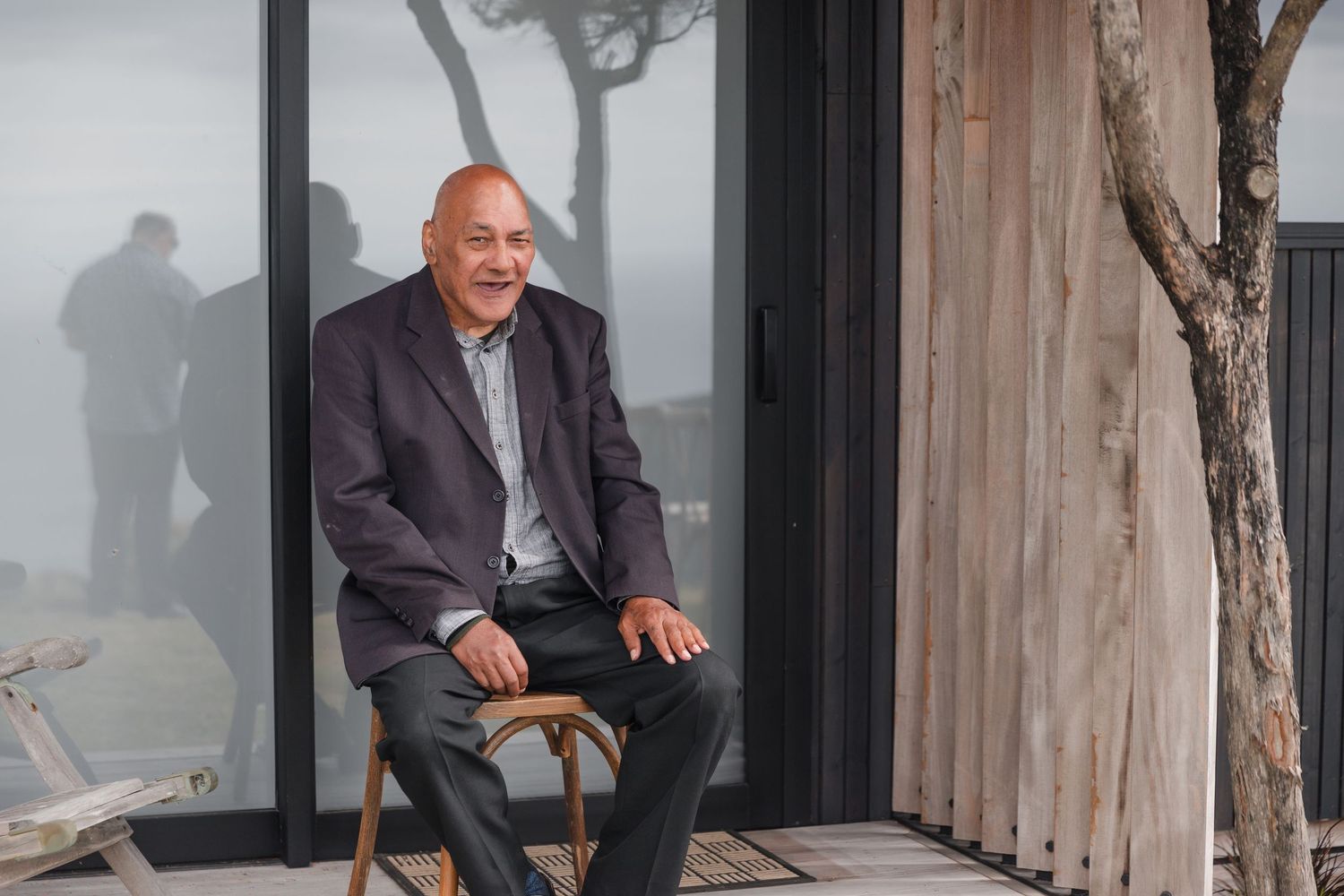 A person sits on a chair outside on a wooden deck with a misty background and tree silhouette visible.