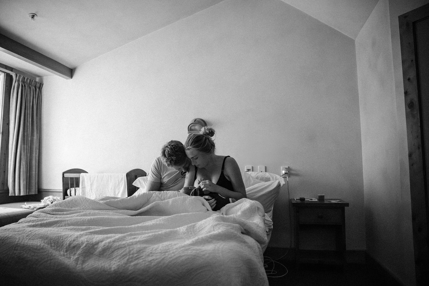 Black and white photo of two women sitting on a bed in a bedroom, sharing an intimate moment.