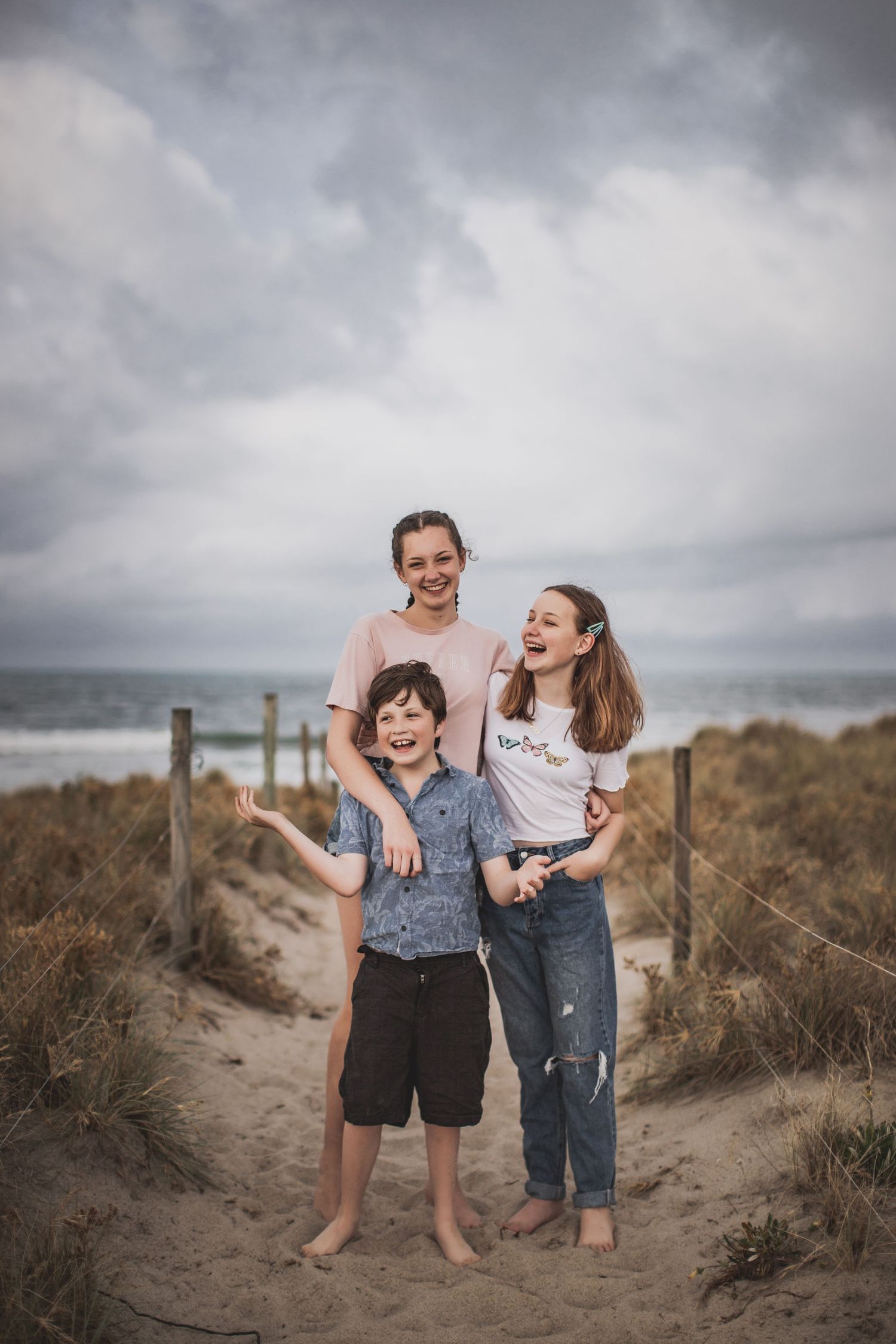 Three siblings share joyful moment together on beach boardwalk with ocean view.