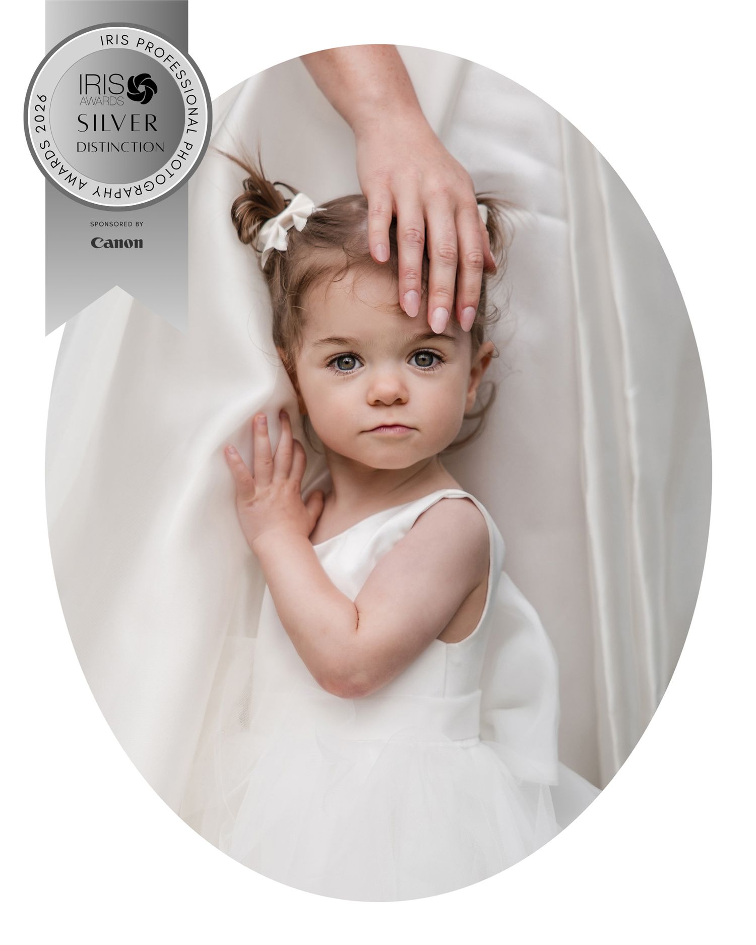 Award-winning portrait of a toddler girl in white dress, gentle hand resting on her head, soft ethereal background.
