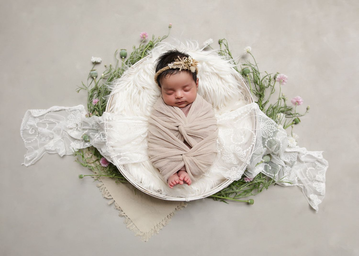 Joyful baby wrapped in neutral fabric lying in white bowl with floral decorations. Cambridge Waikato NZ Photographer
