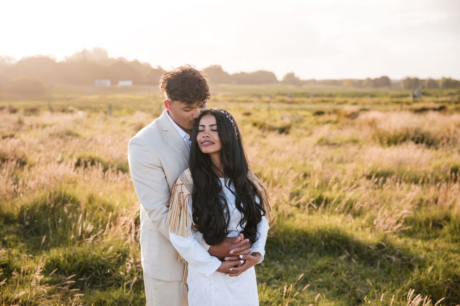A couple shares intimate moments against backdrop of golden sunlit meadows at sunset.
