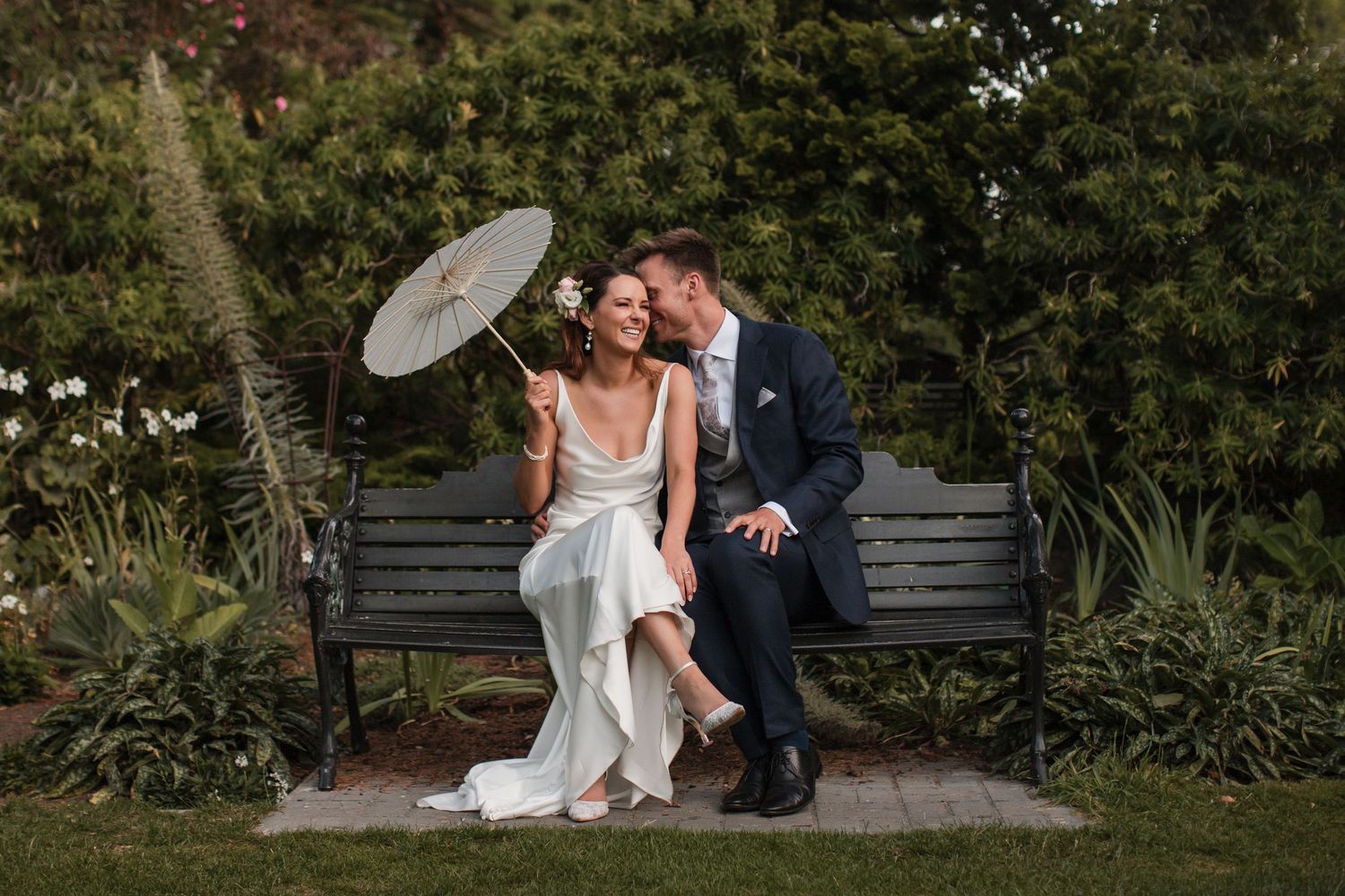 A romantic wedding couple embraces in a lush garden setting during an outdoor photo session.