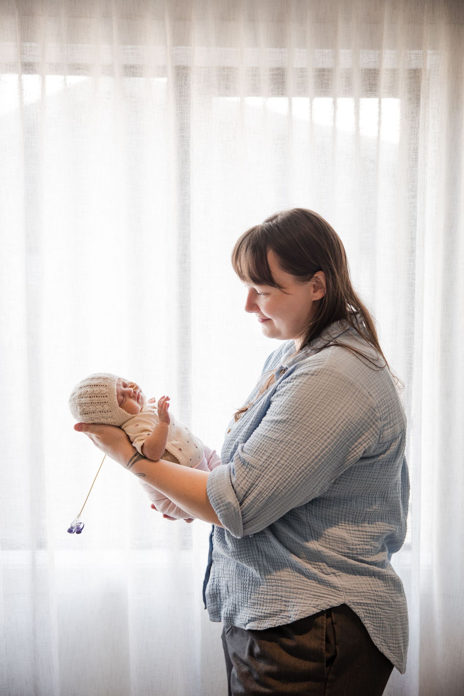 A mother tenderly holds her newborn baby near a bright window.