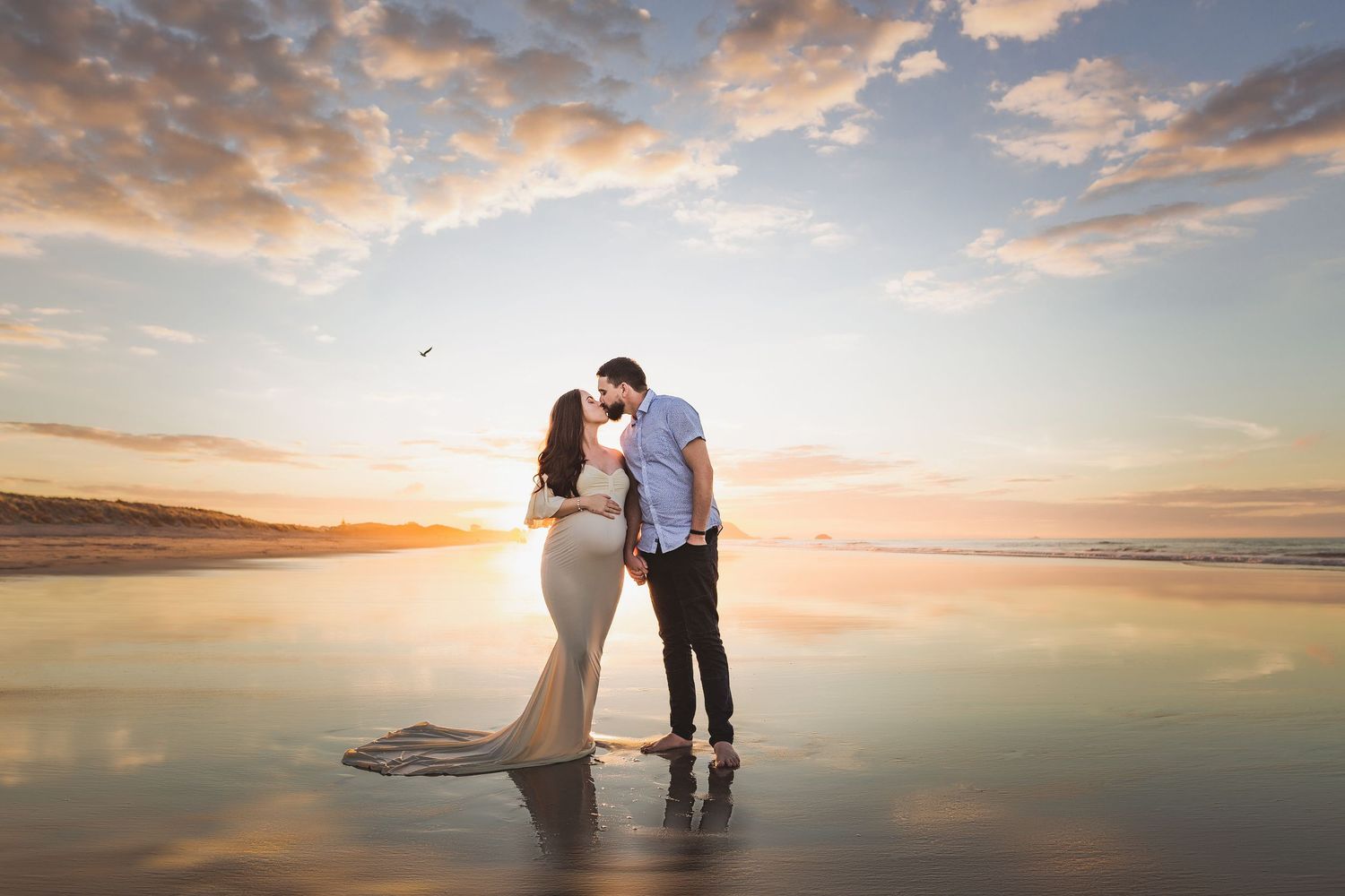 A couple shares an intimate moment on a beach at sunset with dramatic clouds overhead. Cambridge Waikato NZ Photographer. White Locket