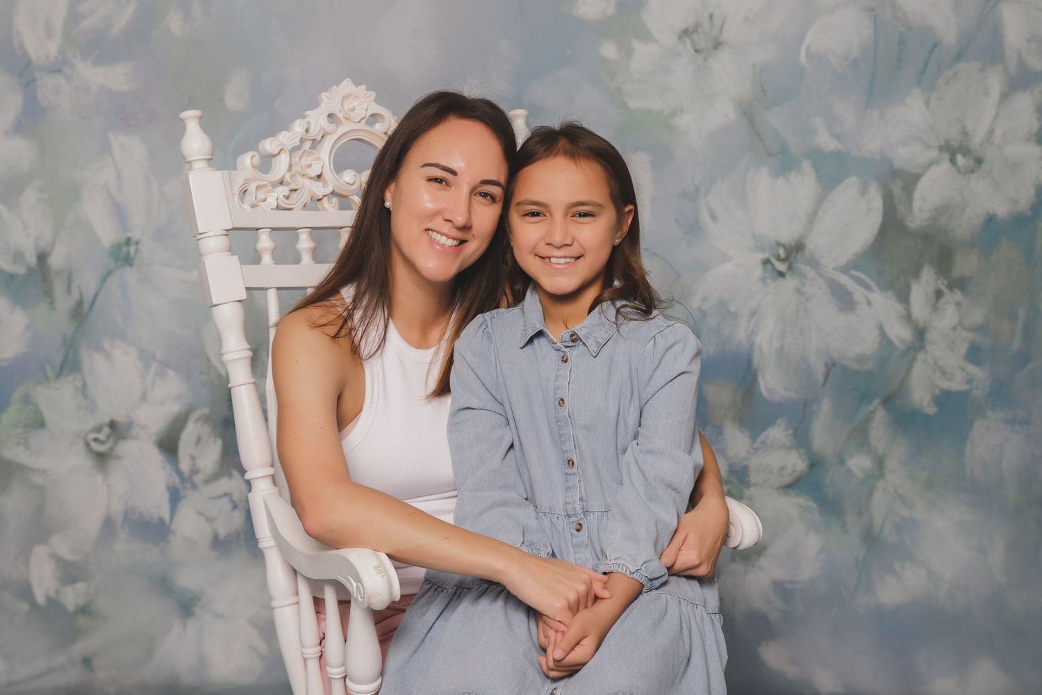 Two people pose and smile together against a floral background in white and blue outfits.