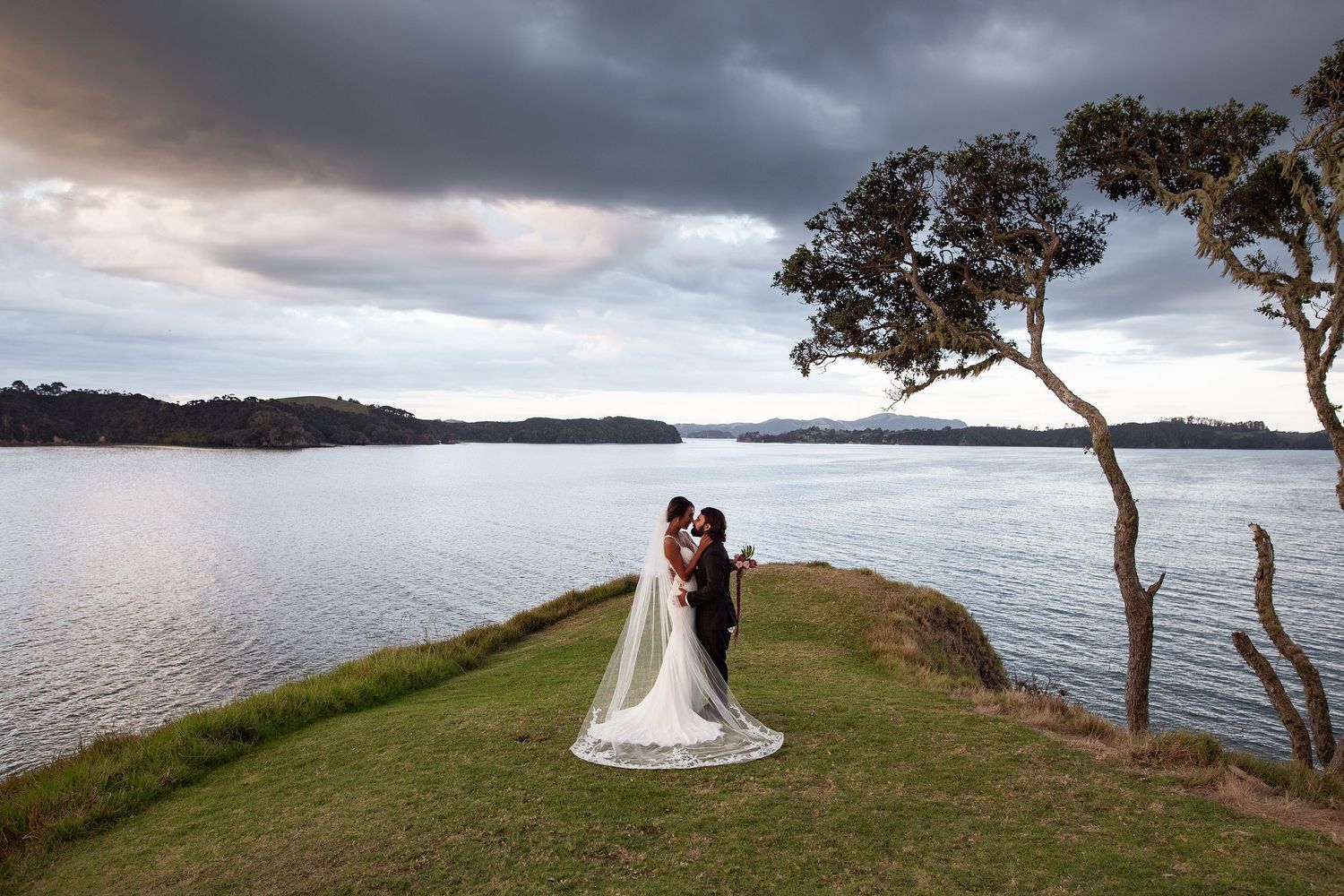 Dramatic moody sky over a coastal landscape with trees and water at dusk.