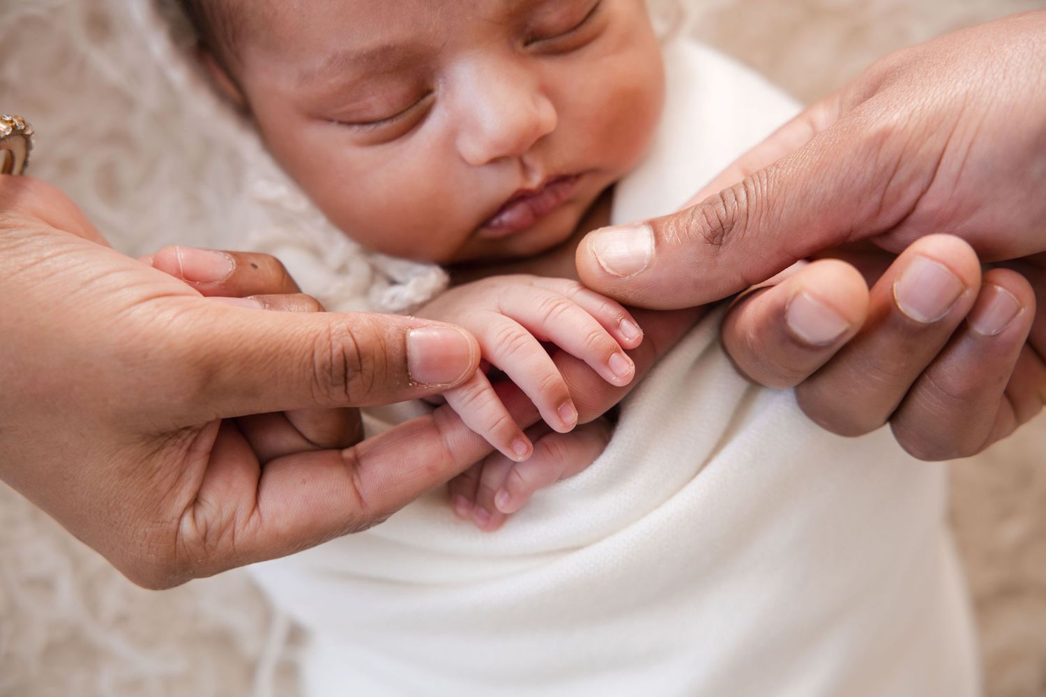 Close up of gentle hands holding a sleeping newborn baby's tiny fingers.