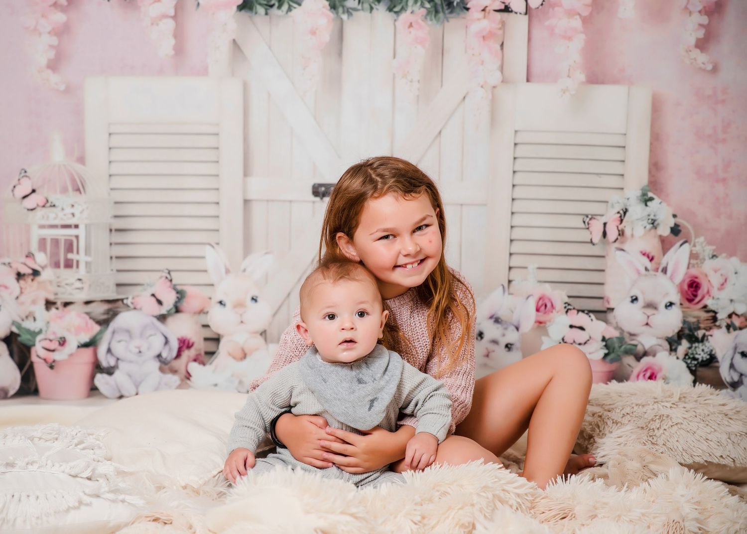 Family together in white studio with pink floral backdrop smiling during professional photo session.