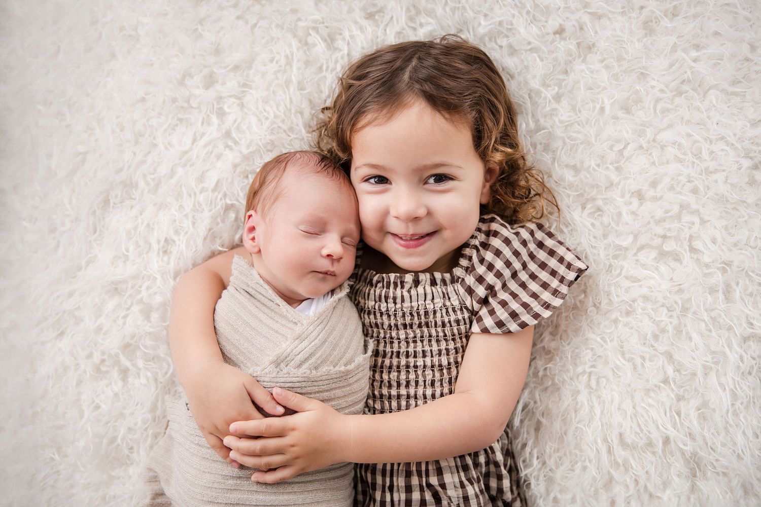 Two children embrace and share sweet moments together in a series of black and white studio portraits on white fabric.