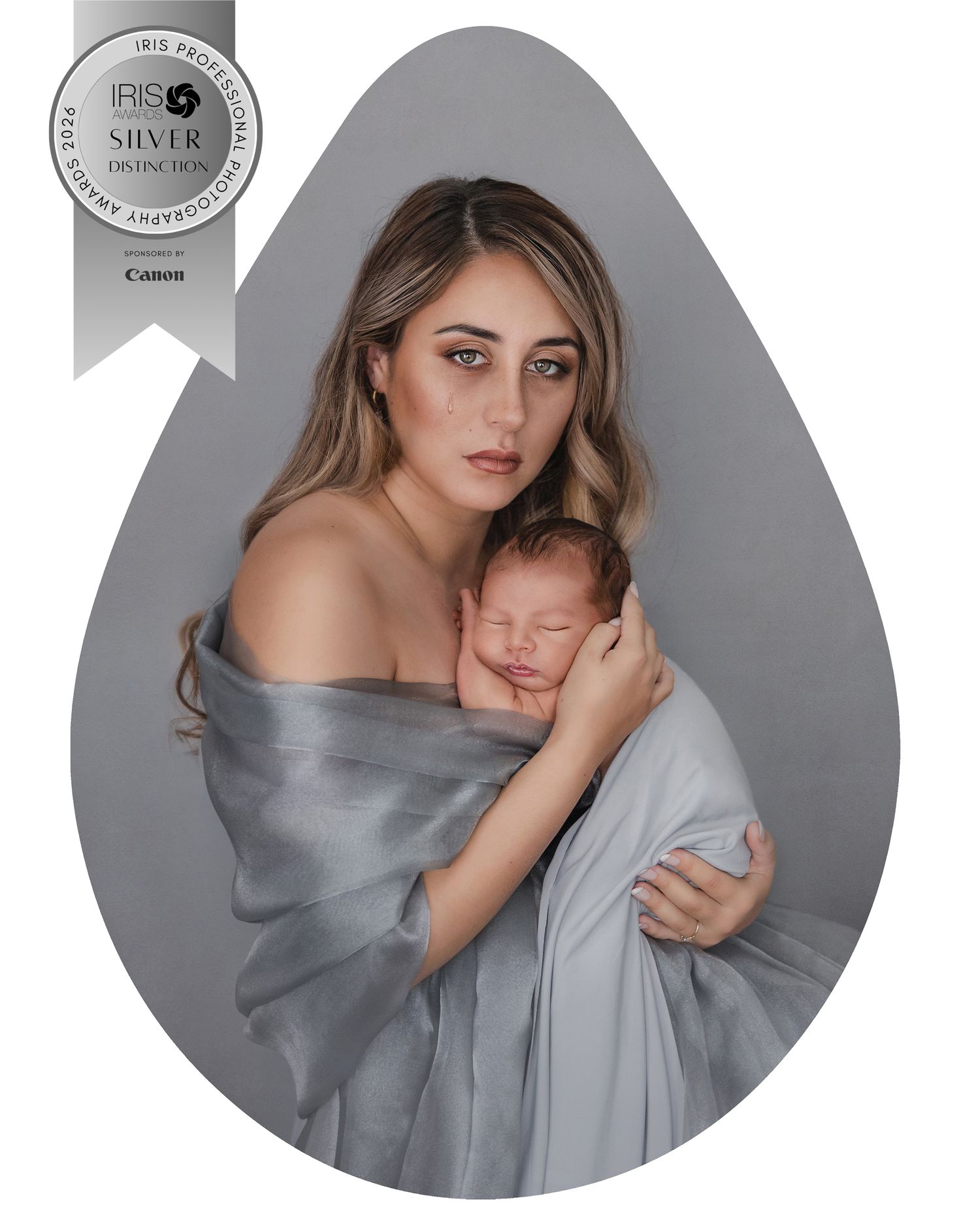 Award-winning portrait of a mother wrapped in silver fabric tenderly holding her sleeping newborn baby.