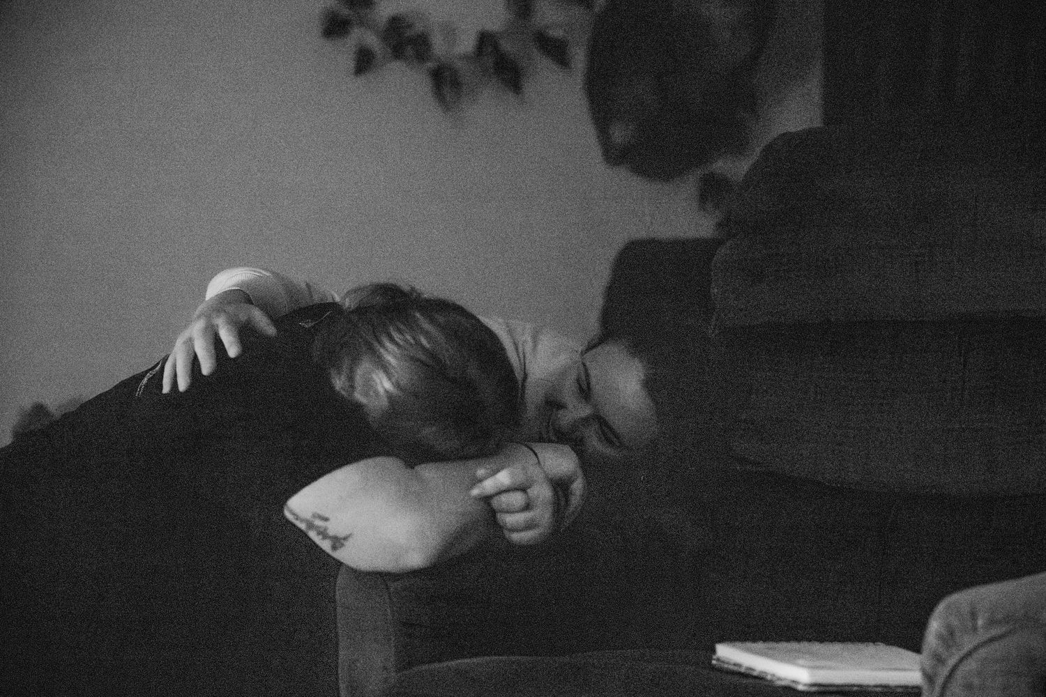 A moody black and white photograph showing someone resting on a couch in a dimly lit room.