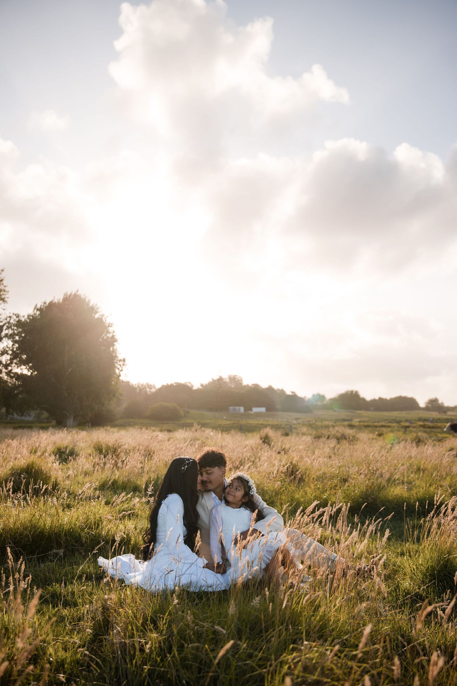 Family sitting together in golden sunlit meadow during sunset photography session.