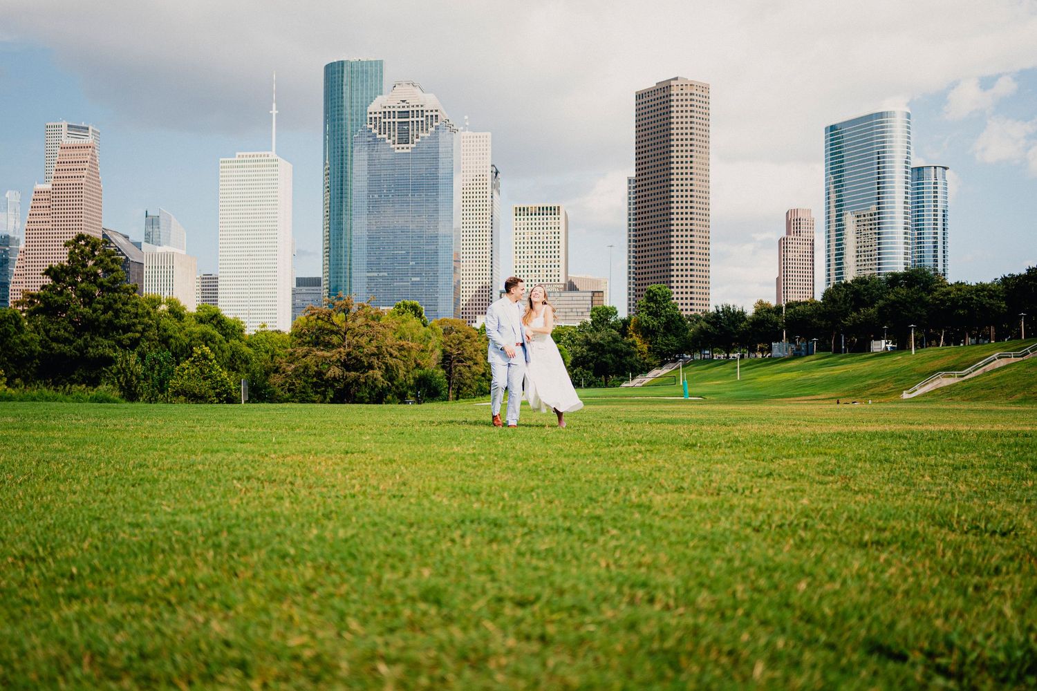 Bride and groom dancing on green lawn with Houston city skyline backdrop on their wedding day.
