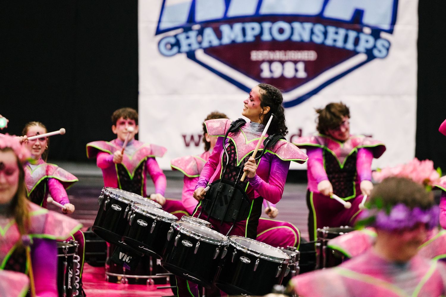 Drummers in bright pink uniforms perform energetically during a championship competition event.