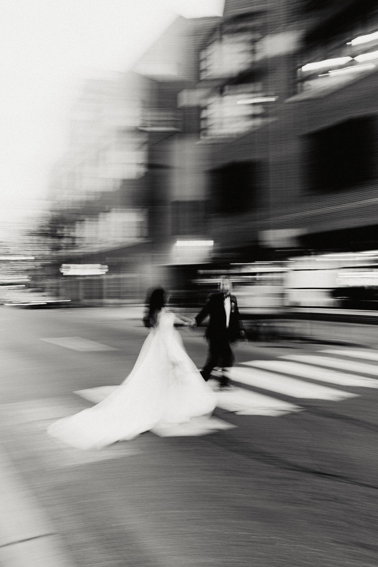 Motion-blurred black and white photograph shows a bride's white dress swirling on a wooden floor during a dance.