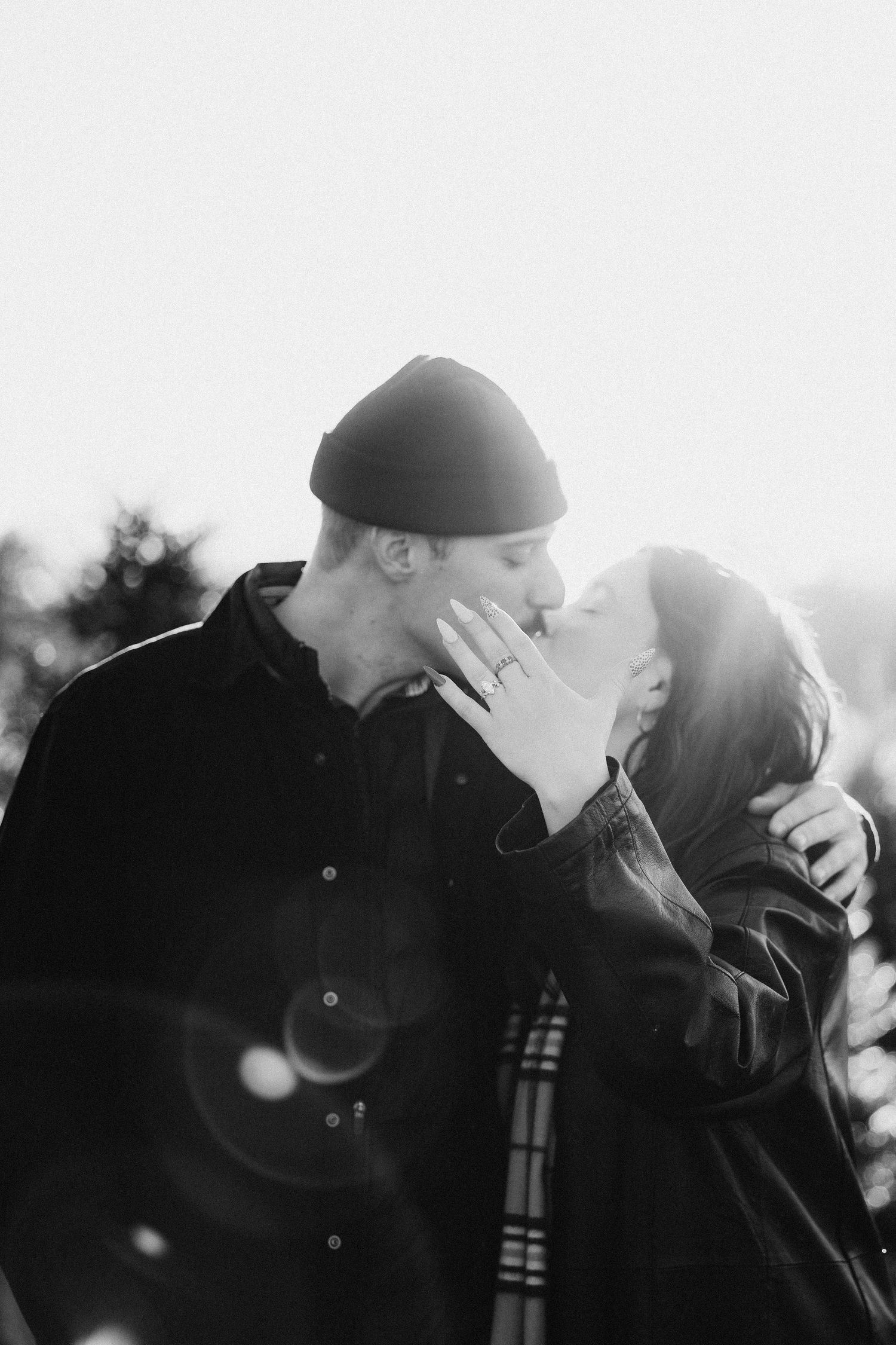 Black and white romantic photo series of couple embracing in sunlit outdoor setting with lens flare effects.