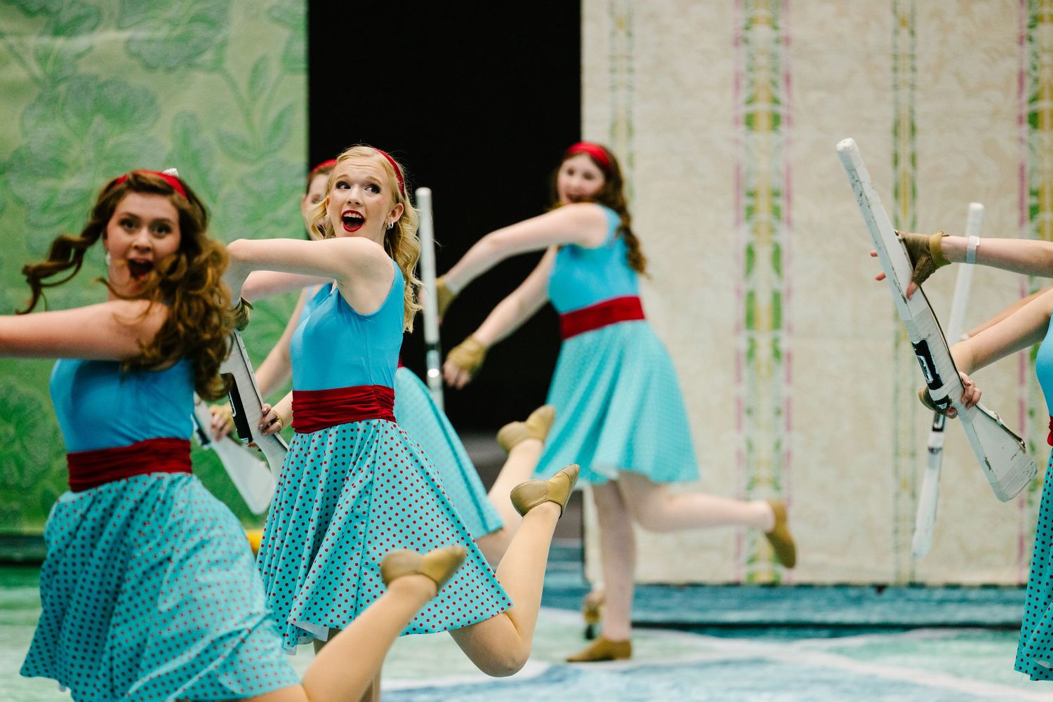 Dancers in matching turquoise dresses perform synchronized movements during a dance routine.