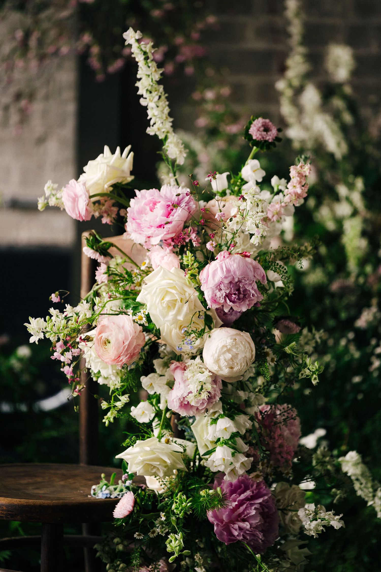 Romantic floral arrangement with pink and white peonies, delicate greenery, and soft blooms against a dark background.