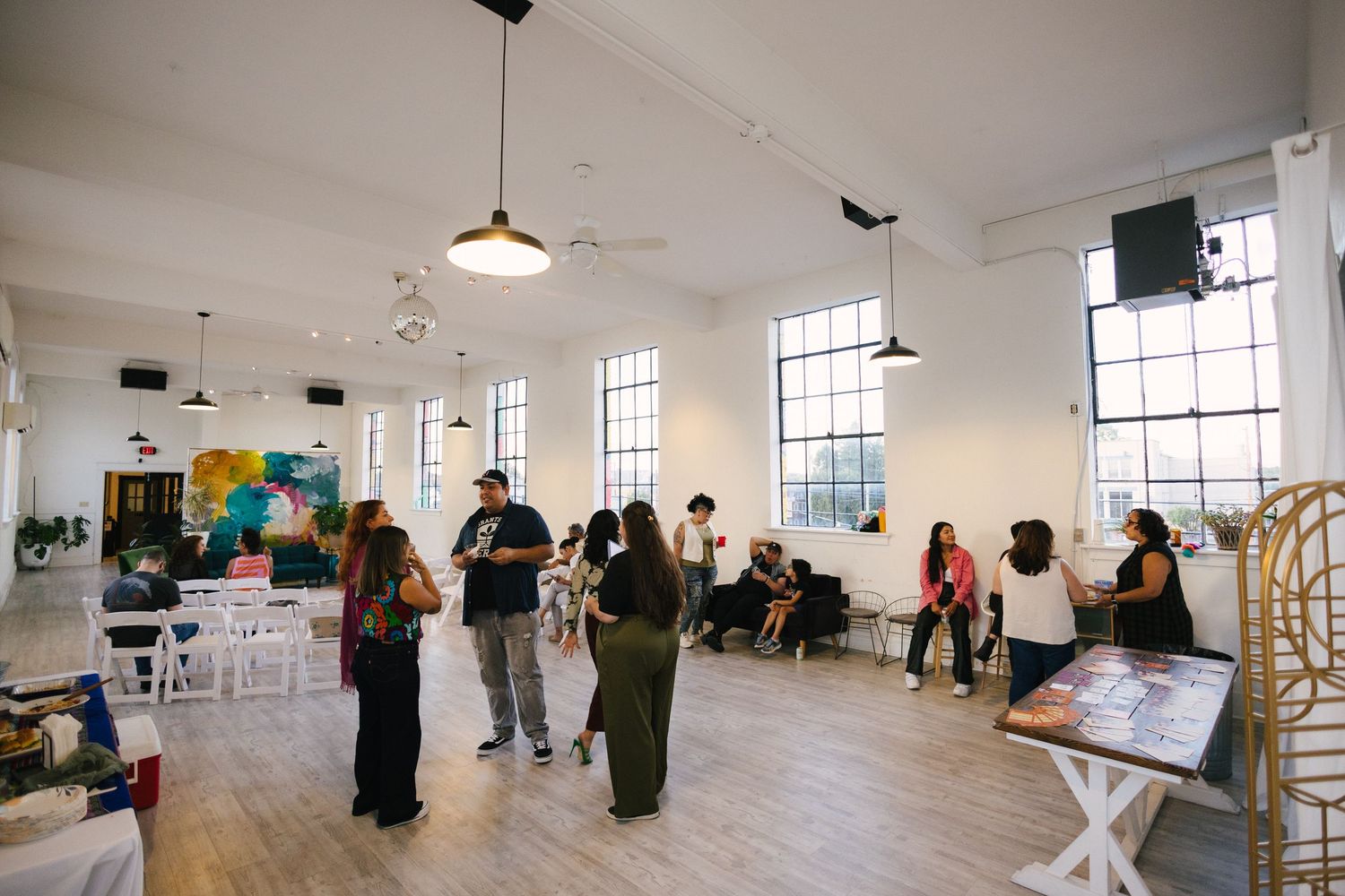 A bright white art gallery or studio space with large windows and people walking through the open interior.