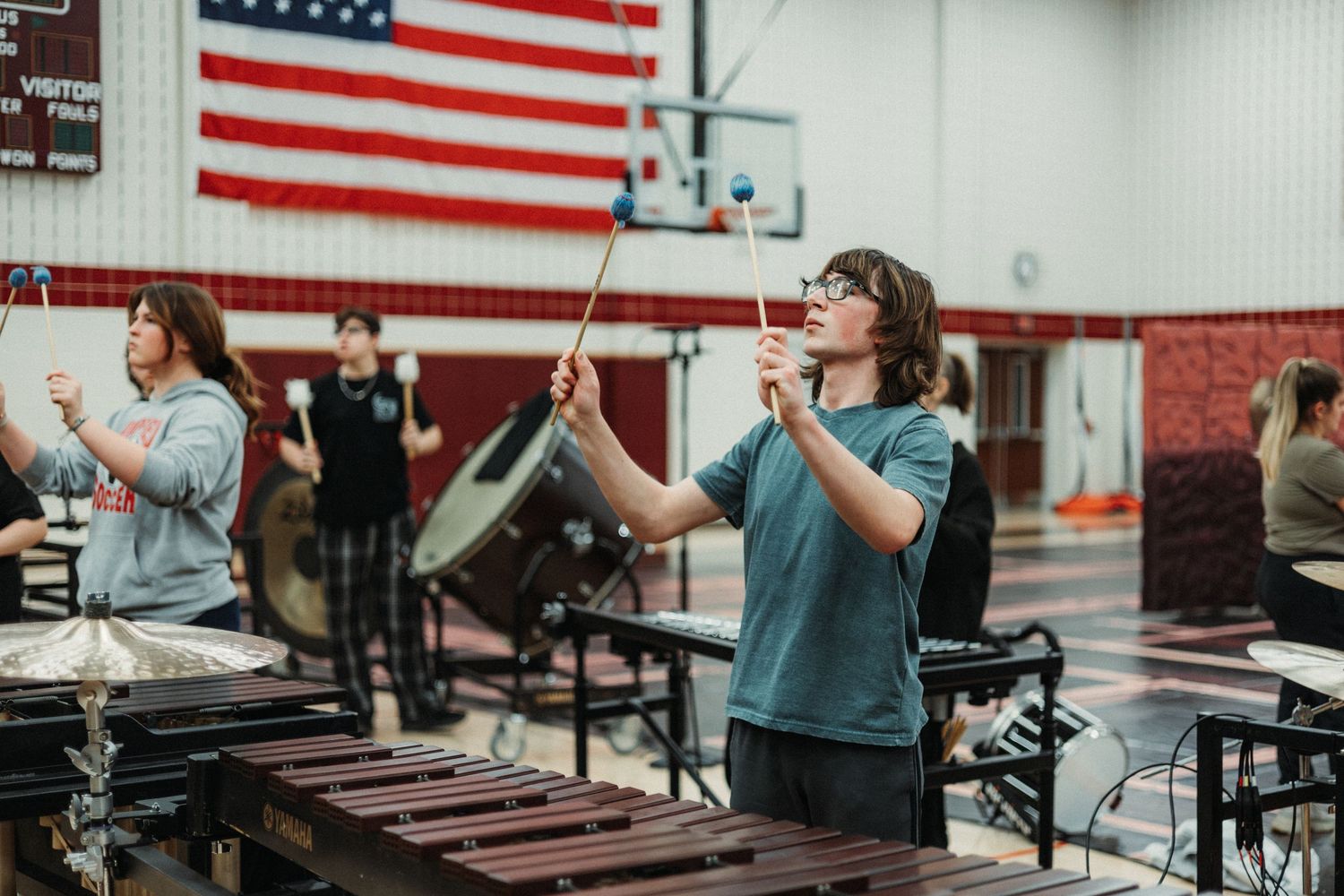 Students practice playing xylophones in a music classroom with an American flag hanging on the wall.
