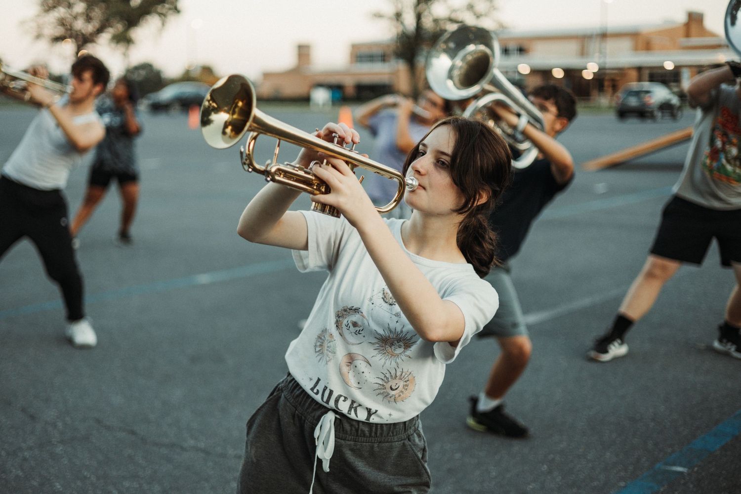 Marching band members practicing formations outdoors at dusk.
