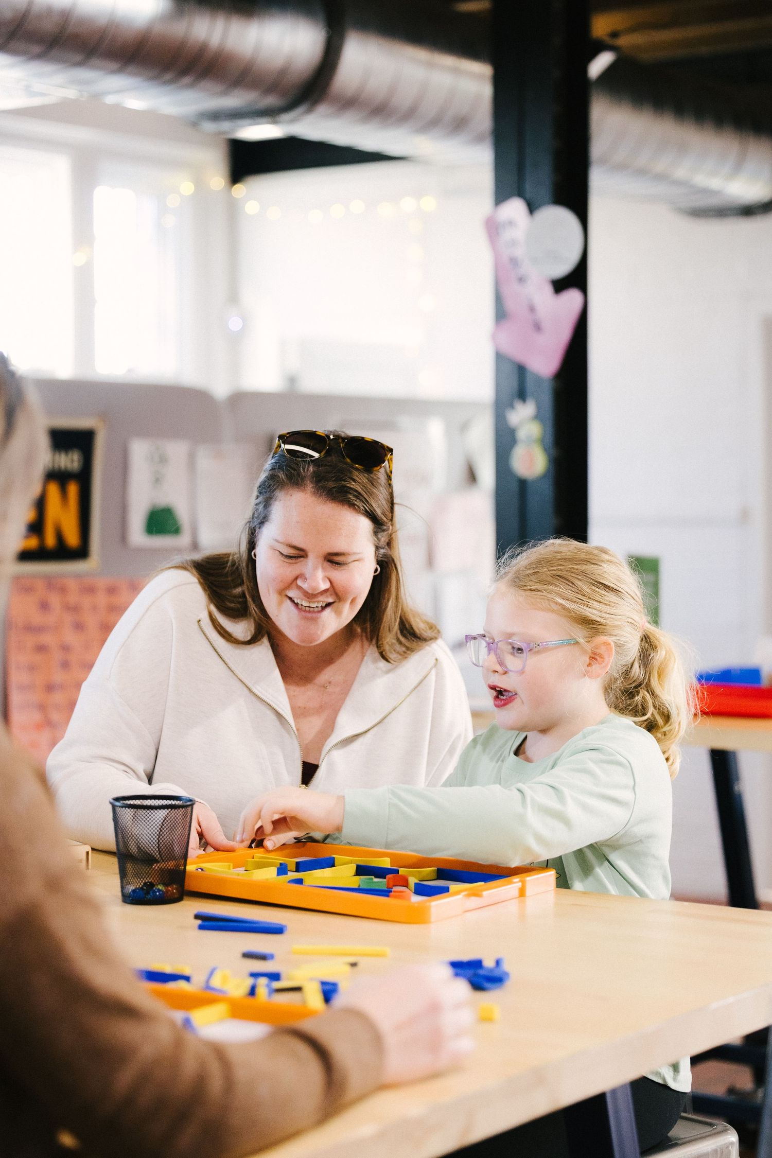 Two people sit at a table working together with colorful learning materials spread out between them.