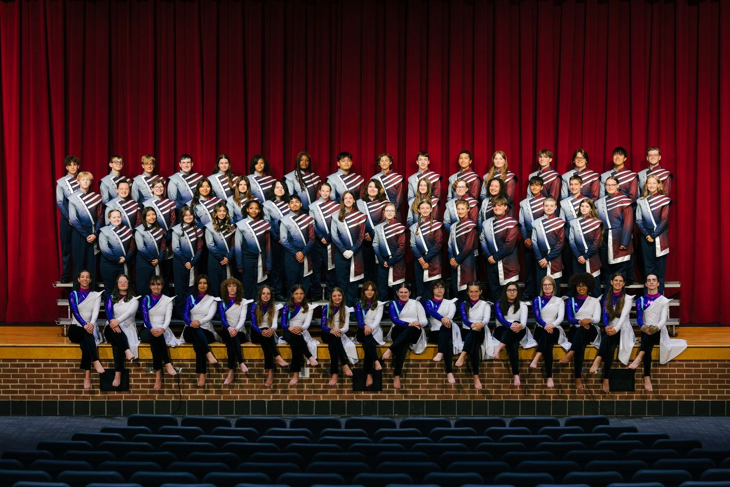 Large group performance on stage with red curtain backdrop.