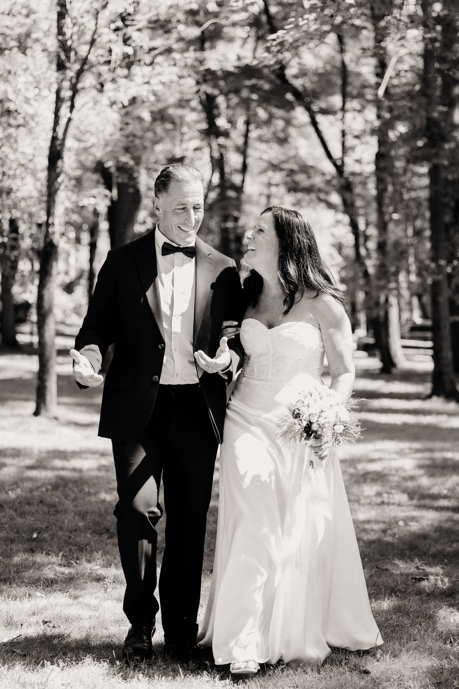 A romantic black and white wedding photo series showing a couple in formal attire walking together outdoors among trees.