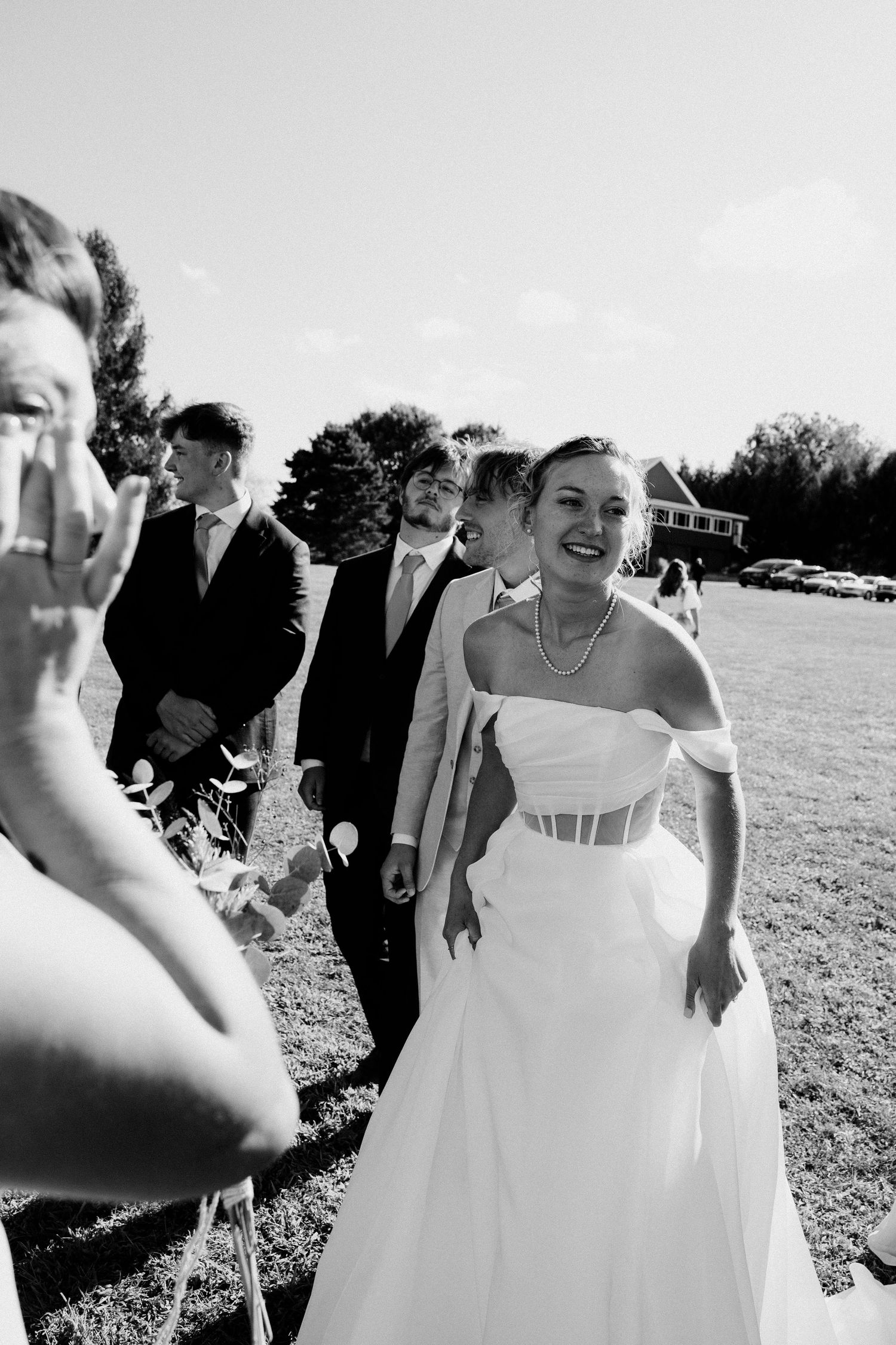 Joyful wedding celebration with guests and bride dancing outdoors in natural lighting.