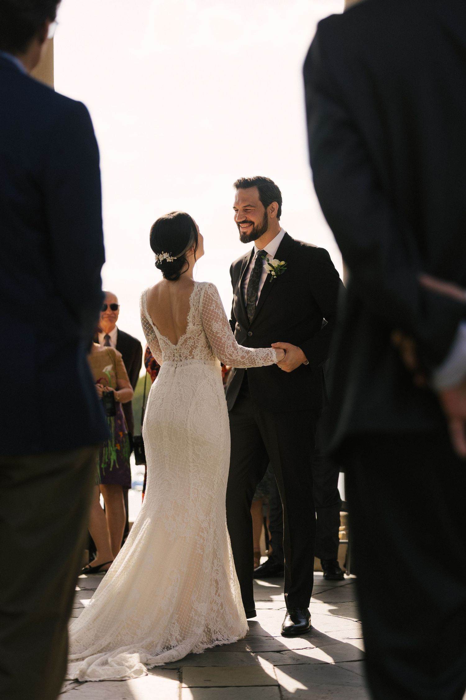A couple in wedding attire share a joyful moment during their celebration as sunlight streams through windows.