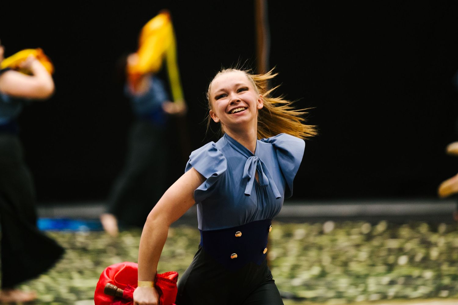 A young woman in a blue top smiles while dancing energetically at a performance event.