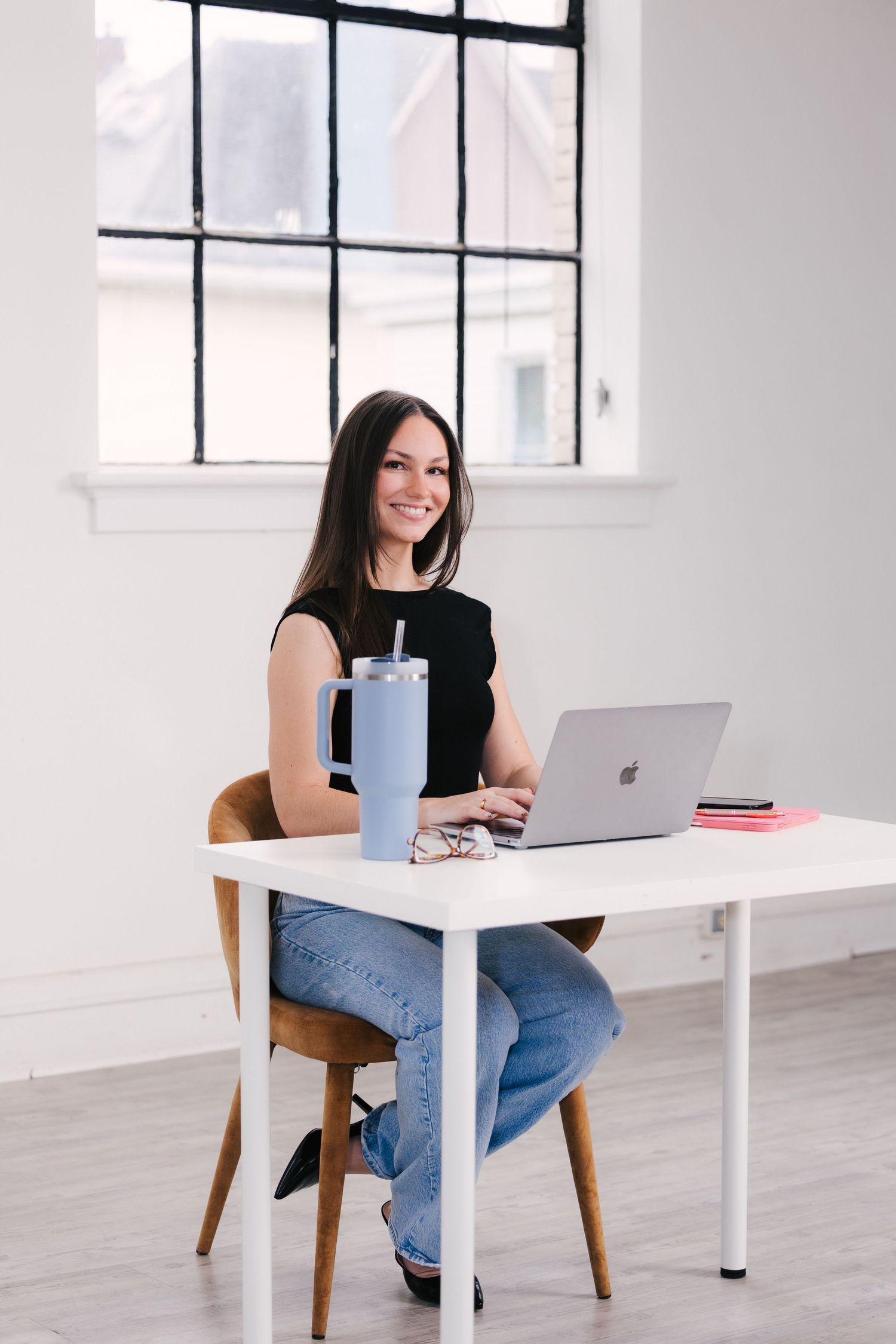 Professional working at modern white desk with laptop and blue coffee mug in bright minimalist office space.
