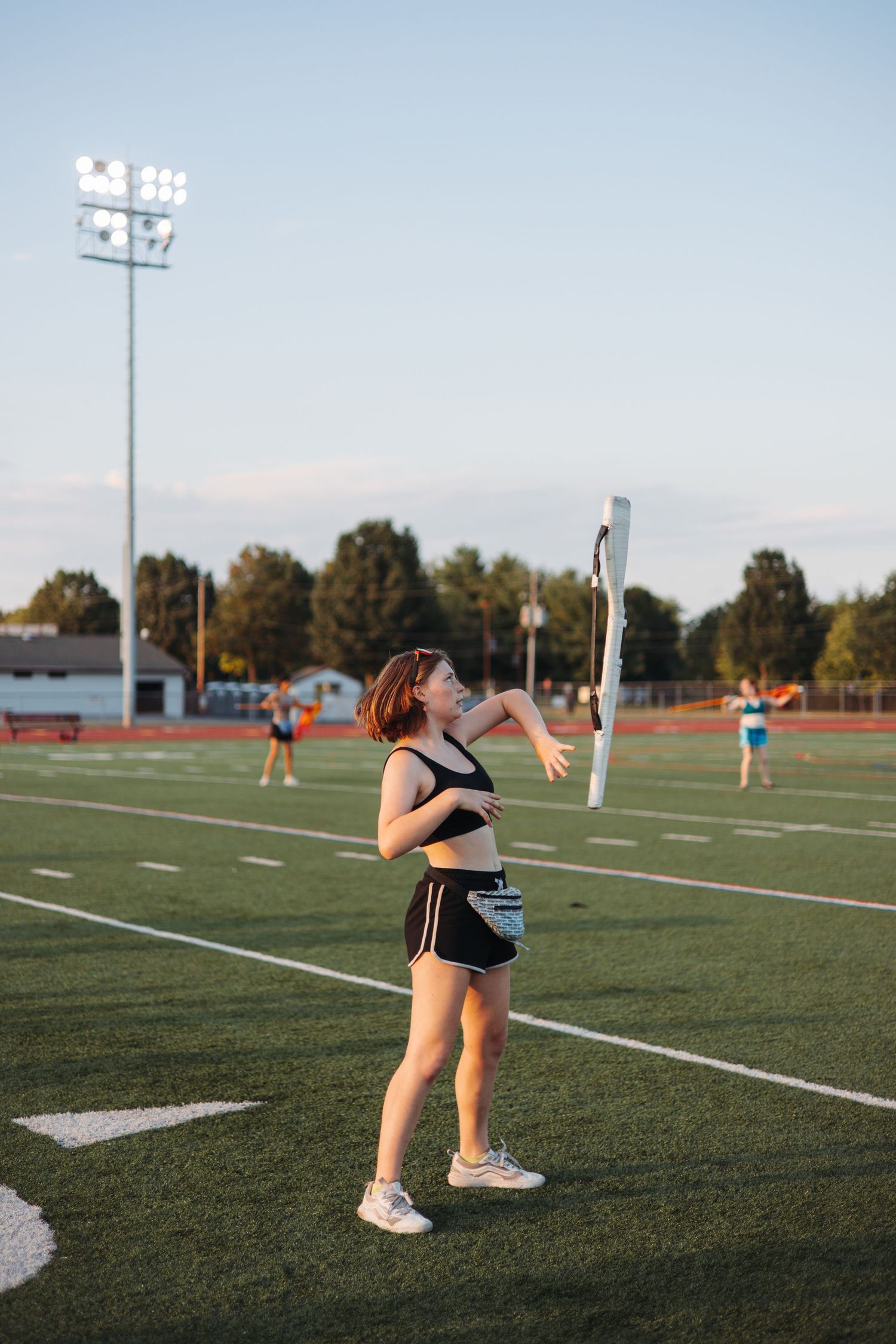 Athletes practicing drills on a football field during sunset.