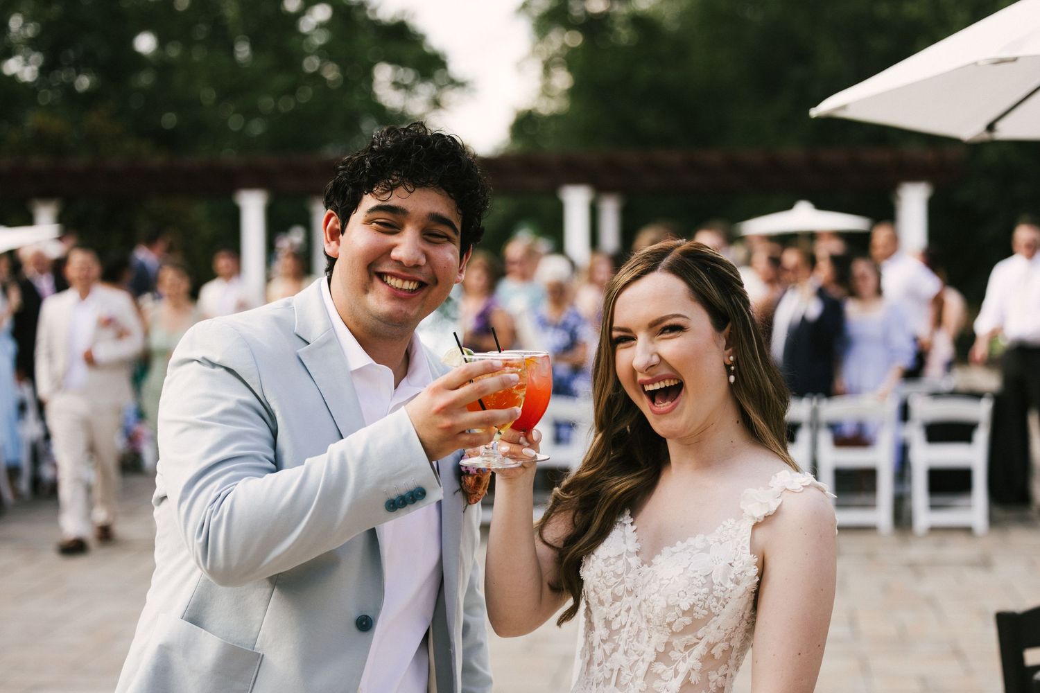 People celebrating and toasting with drinks at an outdoor wedding reception on a sunny day.