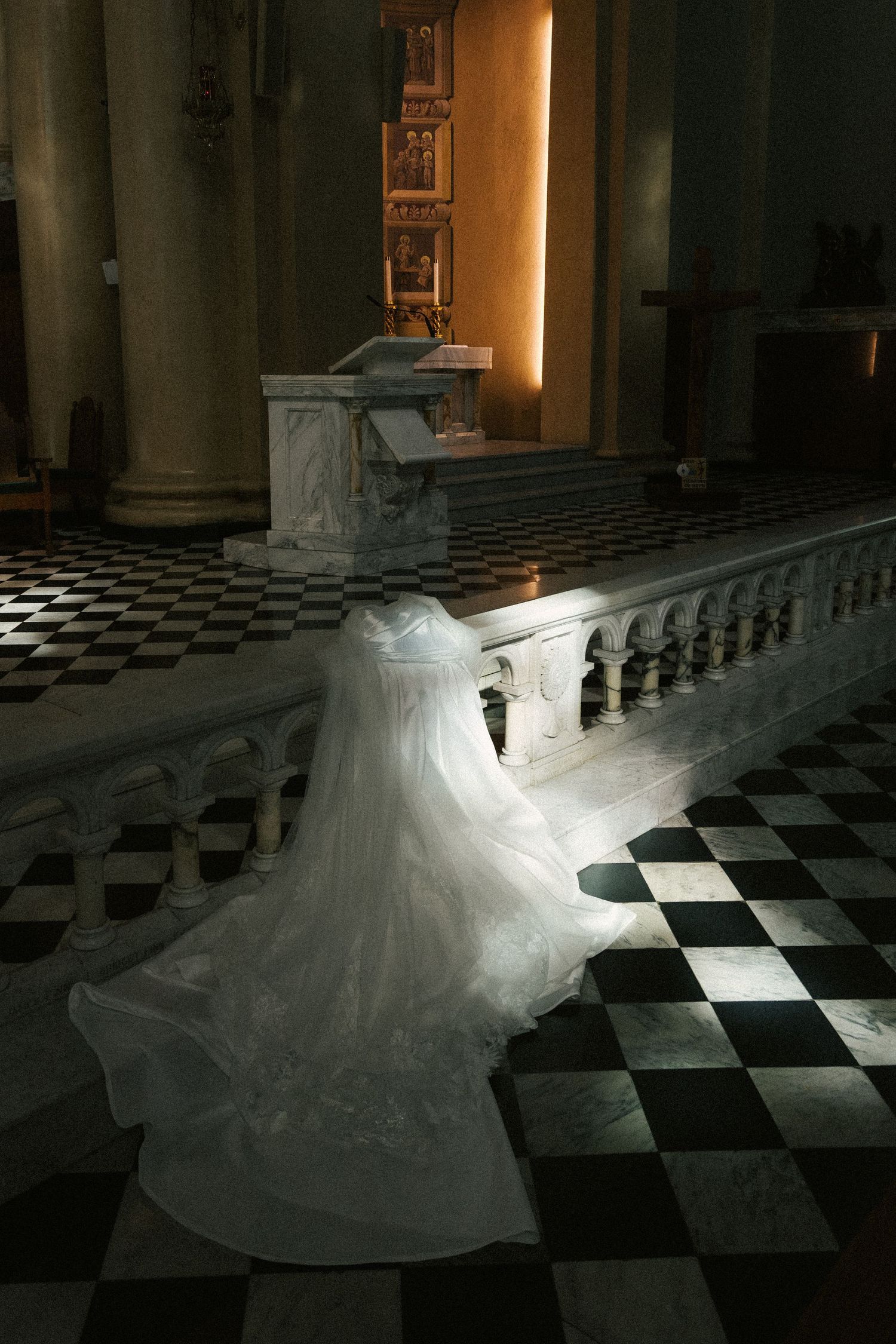 A flowing white wedding dress twirls on a black and white checkered floor in a dimly lit church interior.