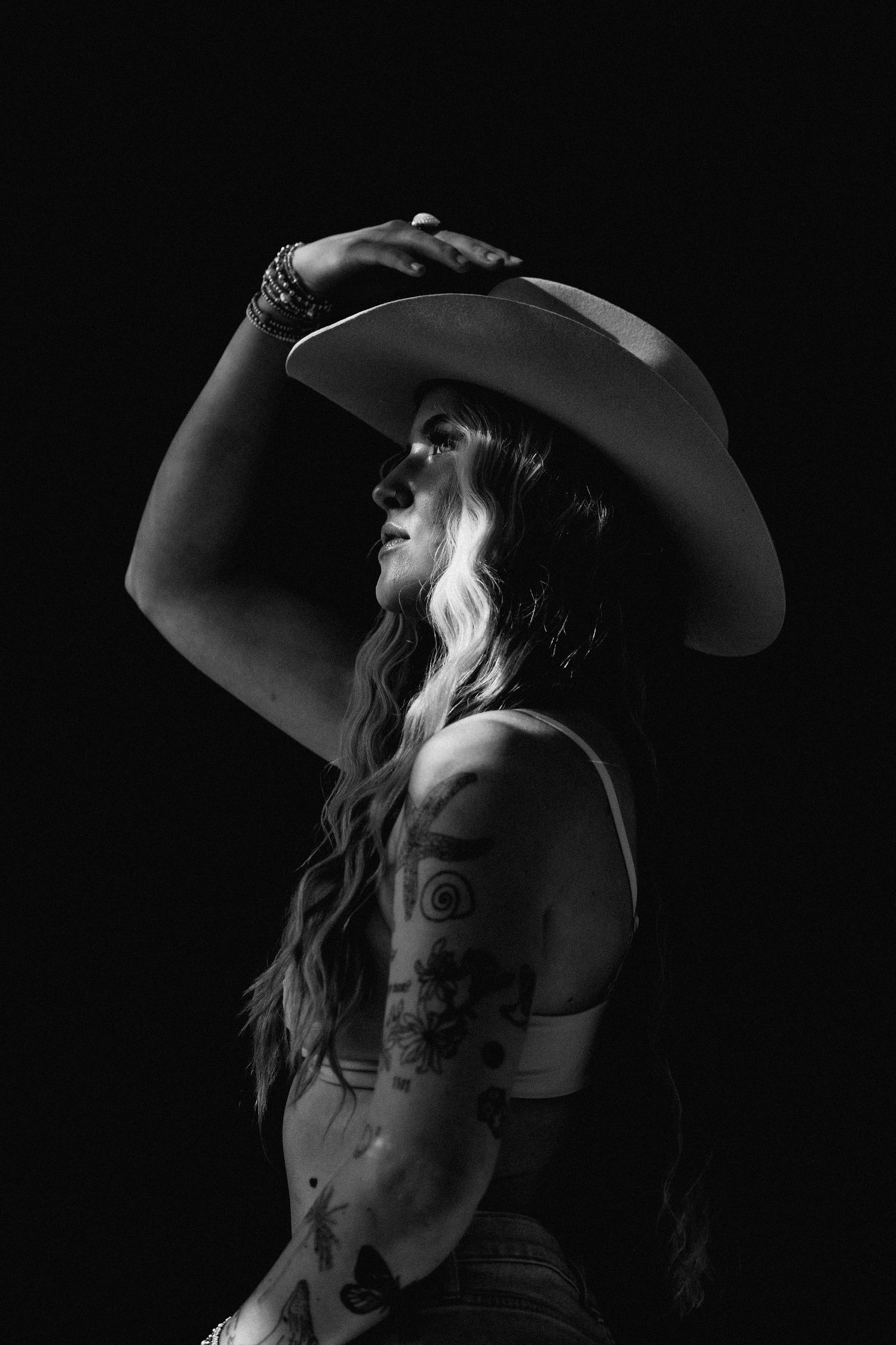 A dramatic black and white portrait of someone in a cowboy hat with flowing hair.