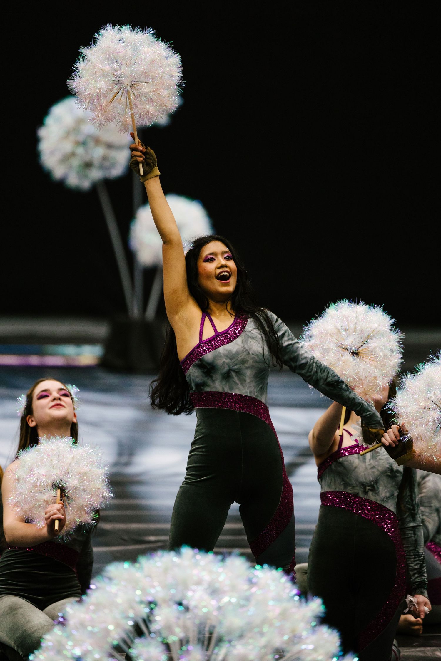 Performance artist with sparkly white pom poms against dark background.